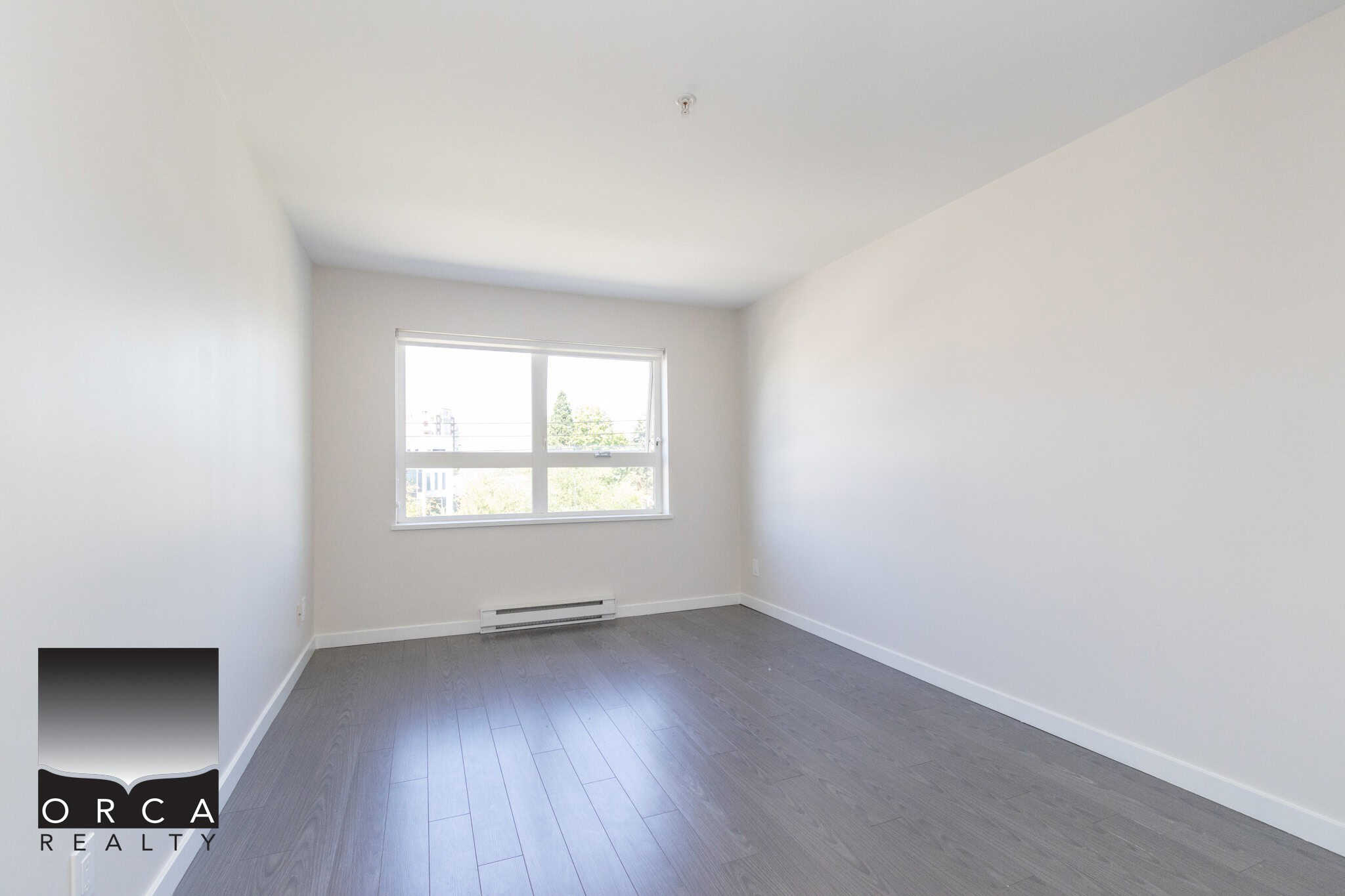 Bright empty bedroom with large window, white walls, and grey laminate flooring, showcasing modern Vancouver real estate for sale by Orca Realty Inc.