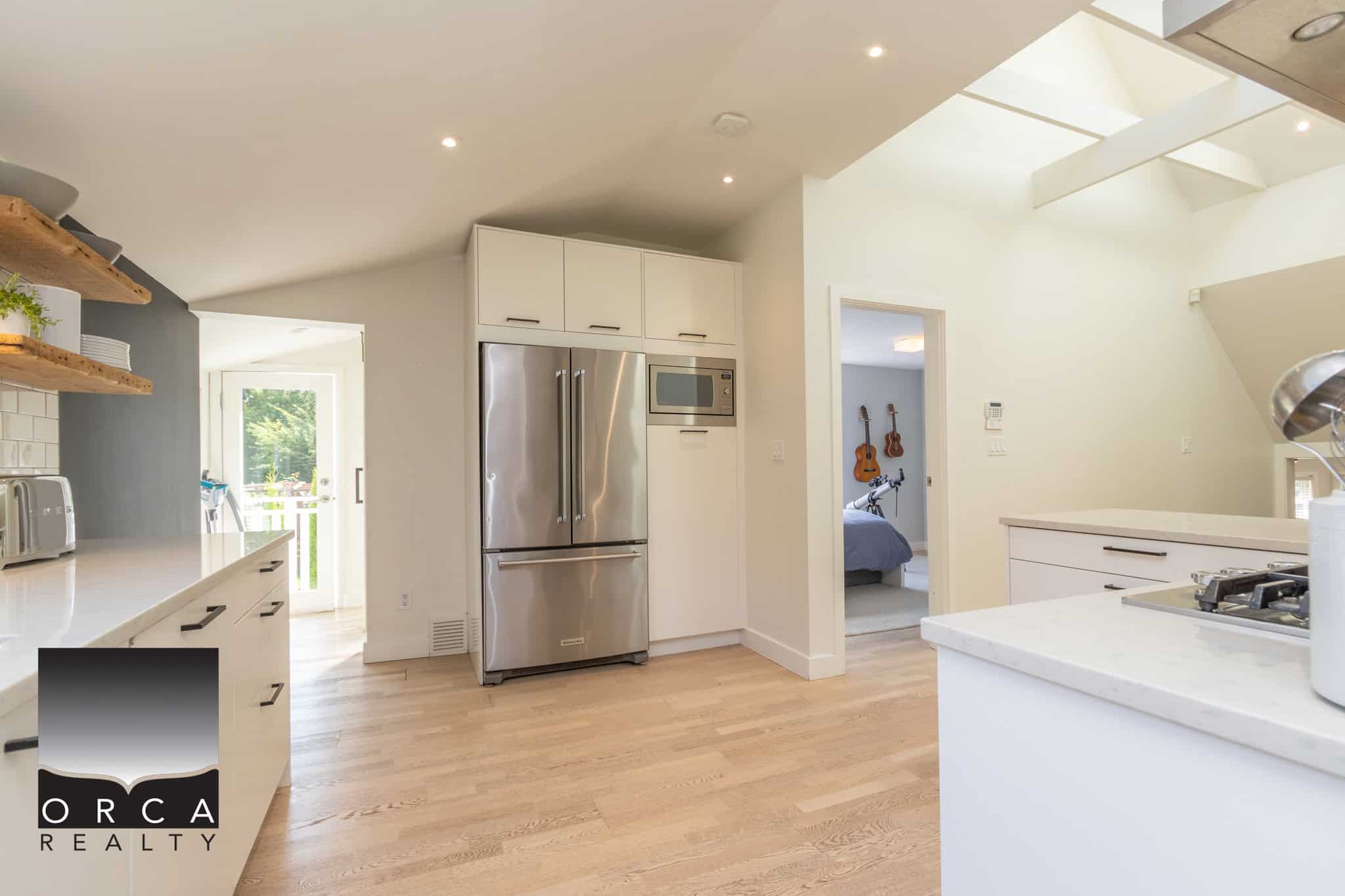 11 Bright modern kitchen with stainless steel appliances, white cabinetry, and natural wood flooring, part of a stylish Vancouver Island home listed by Orca Realty Inc.
