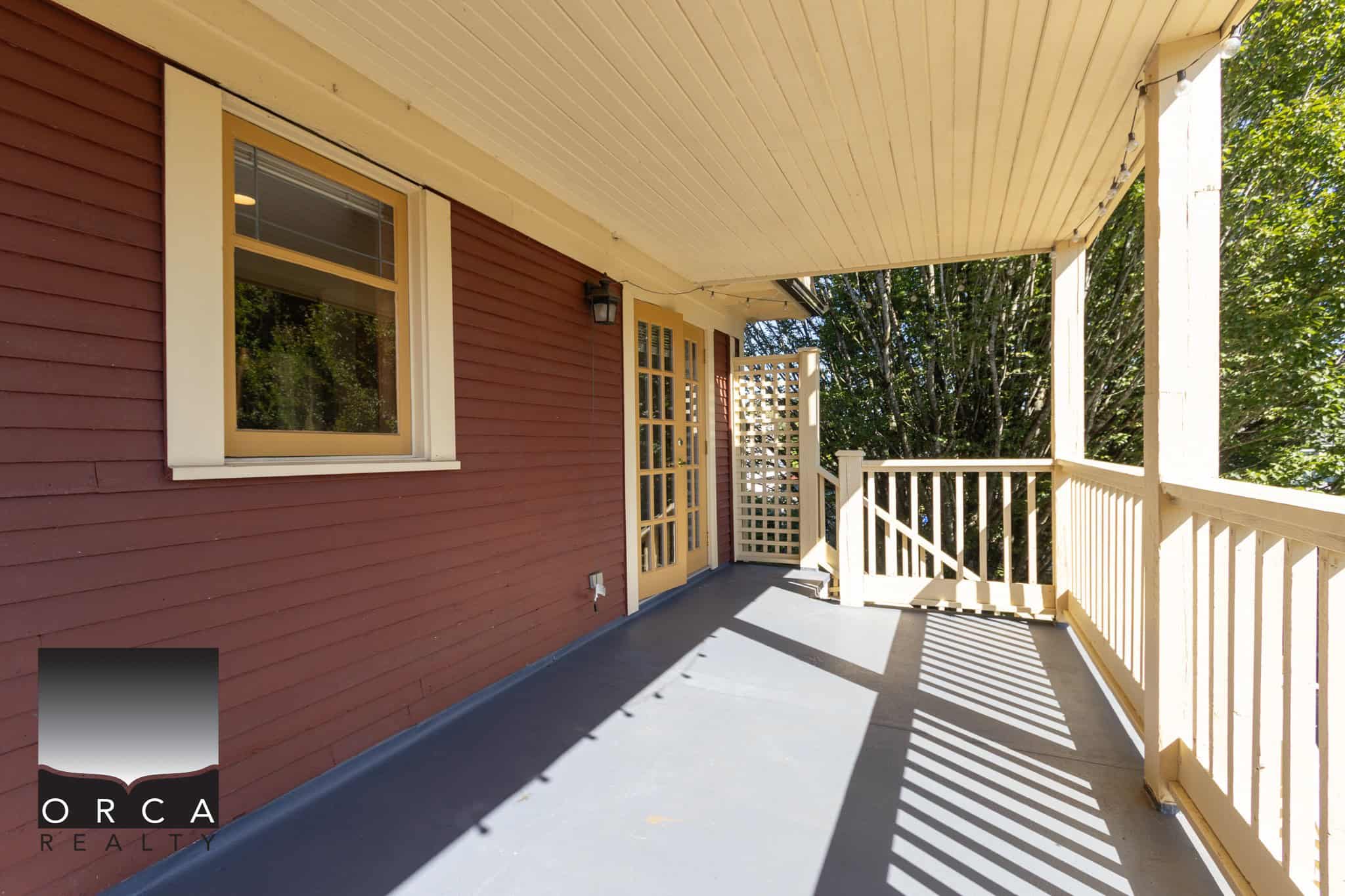 Spacious outdoor balcony with wooden railings, perfect for relaxing and enjoying nature, attached to a charming residential home on a tree-lined street.