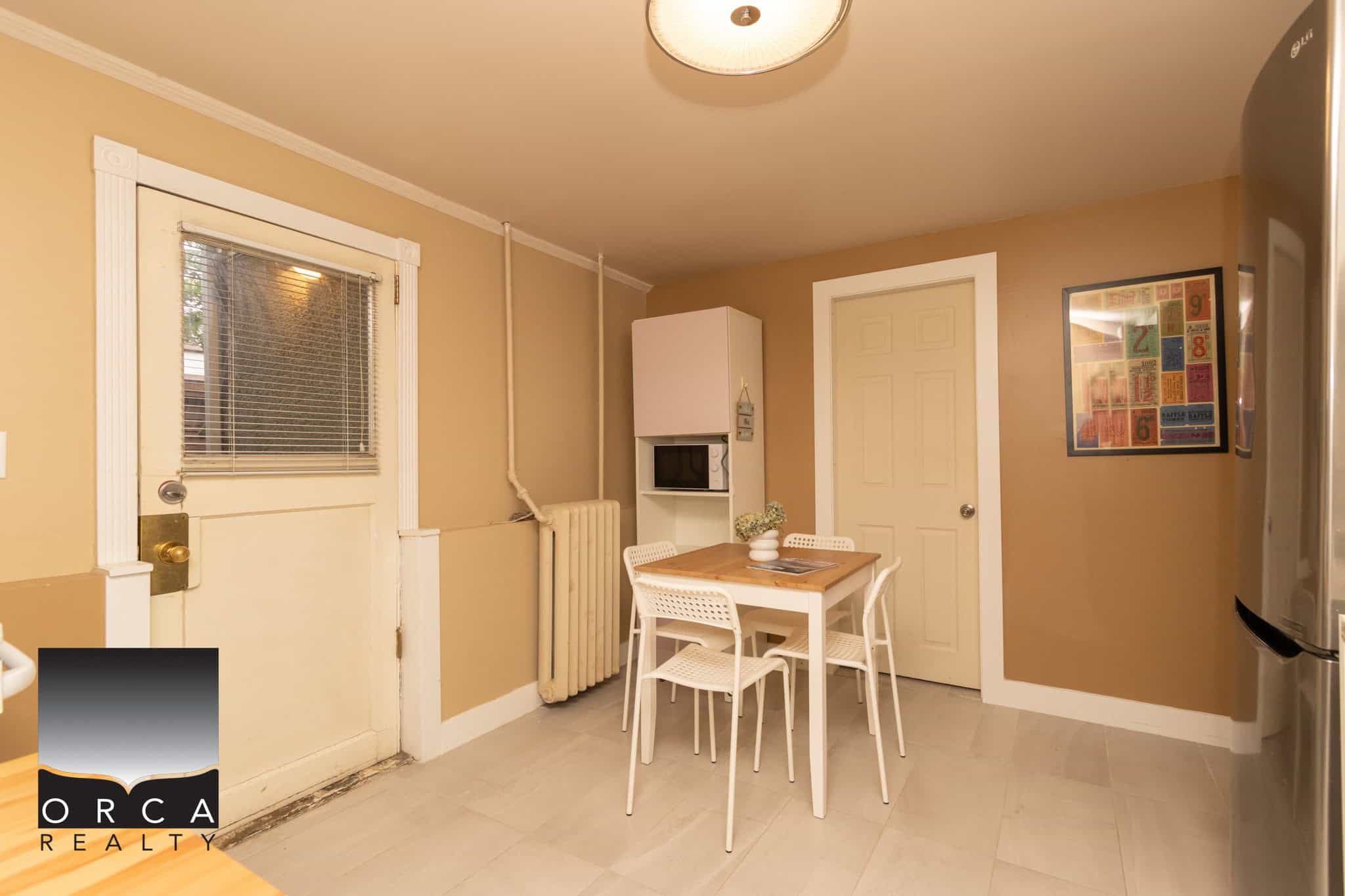 Cozy kitchen dining area with white table and chairs, beige walls, vintage radiator, and modern appliances, perfect for family meals and casual gatherings in a home listed by Orca Realty Inc.