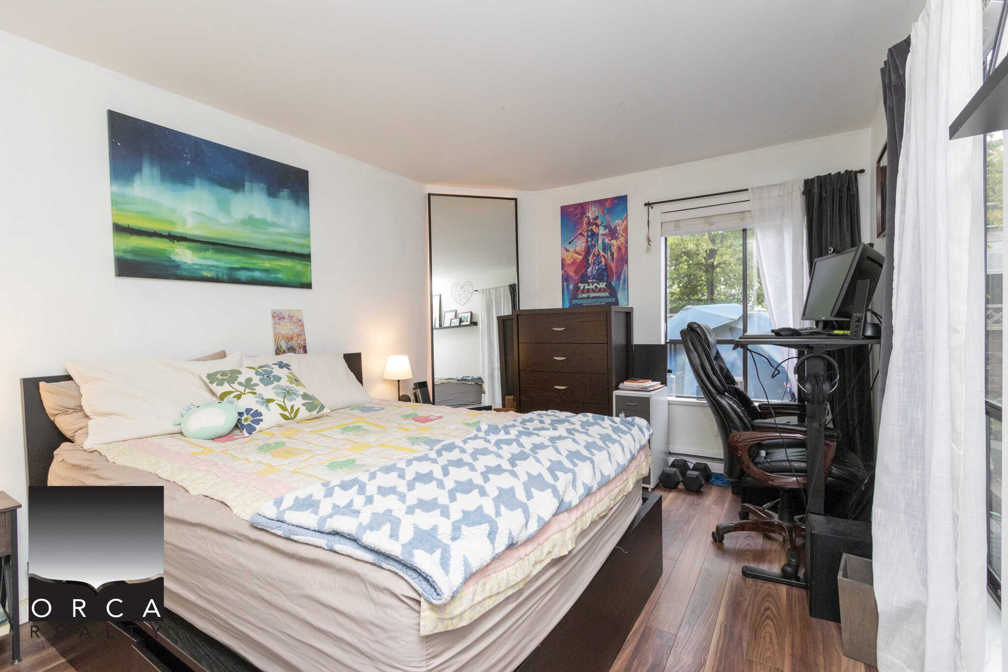 Bright bedroom with a large bed, artwork on the wall, and a workspace with a computer and chair; perfect for relaxation and productivity.