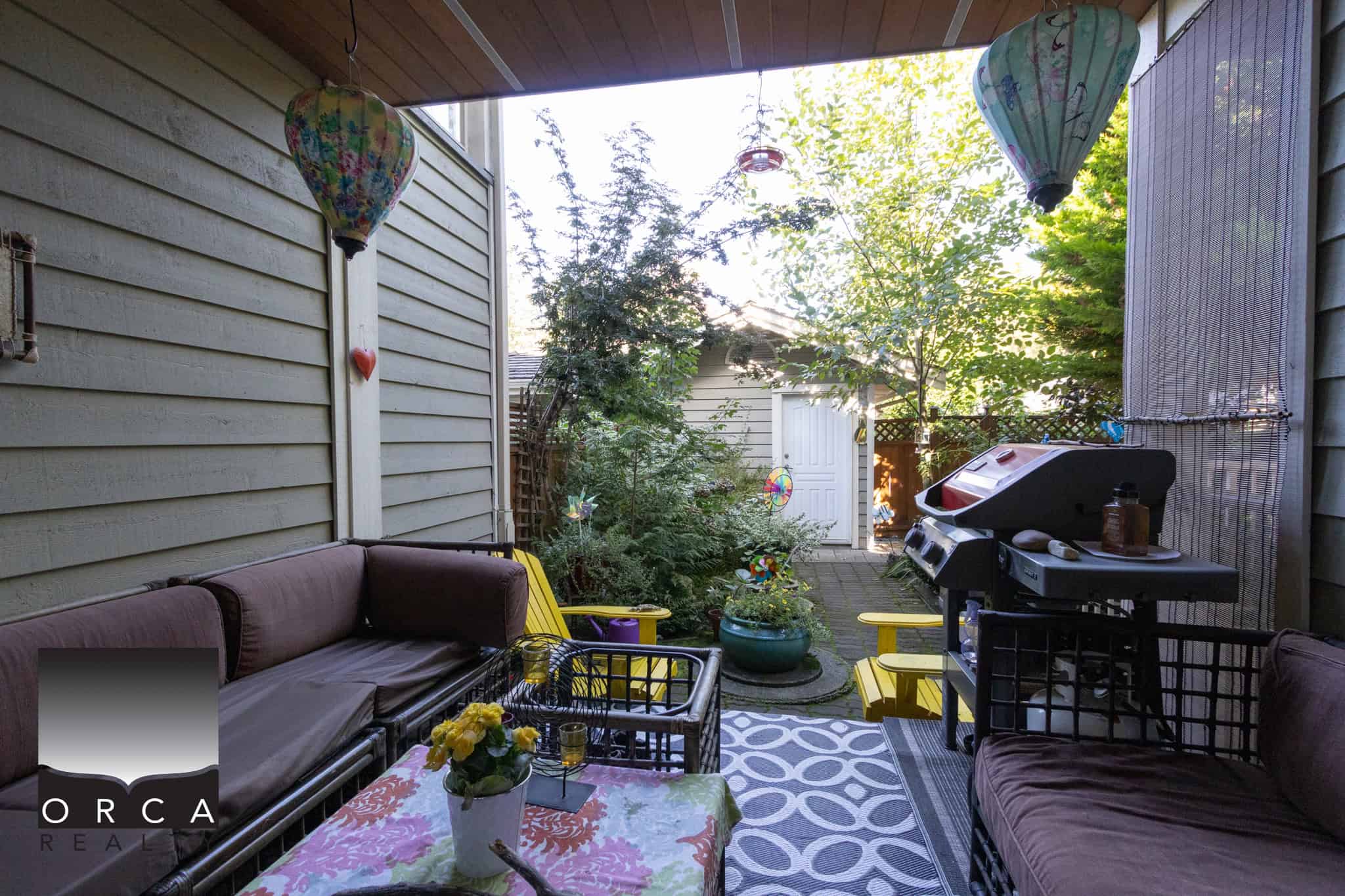 11 Cozy outdoor patio with comfortable seating, colorful lanterns, lush greenery, and a BBQ grill, perfect for relaxing or entertaining in a private backyard setting.