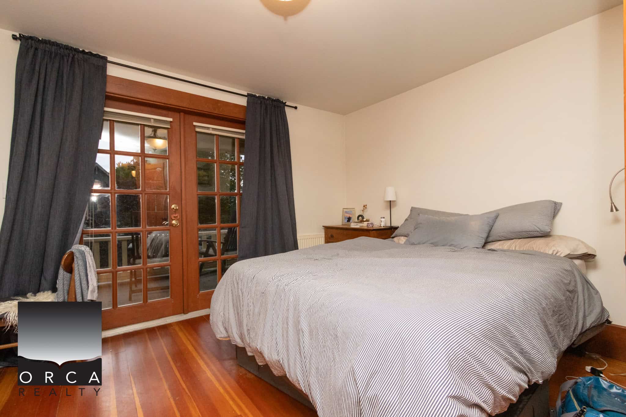 11 Spacious bedroom with wooden floors, large glass doors leading to a patio, dark curtains, and cozy bedding, ideal for showcasing homes listed by Orca Realty Inc. for real estate in BC.