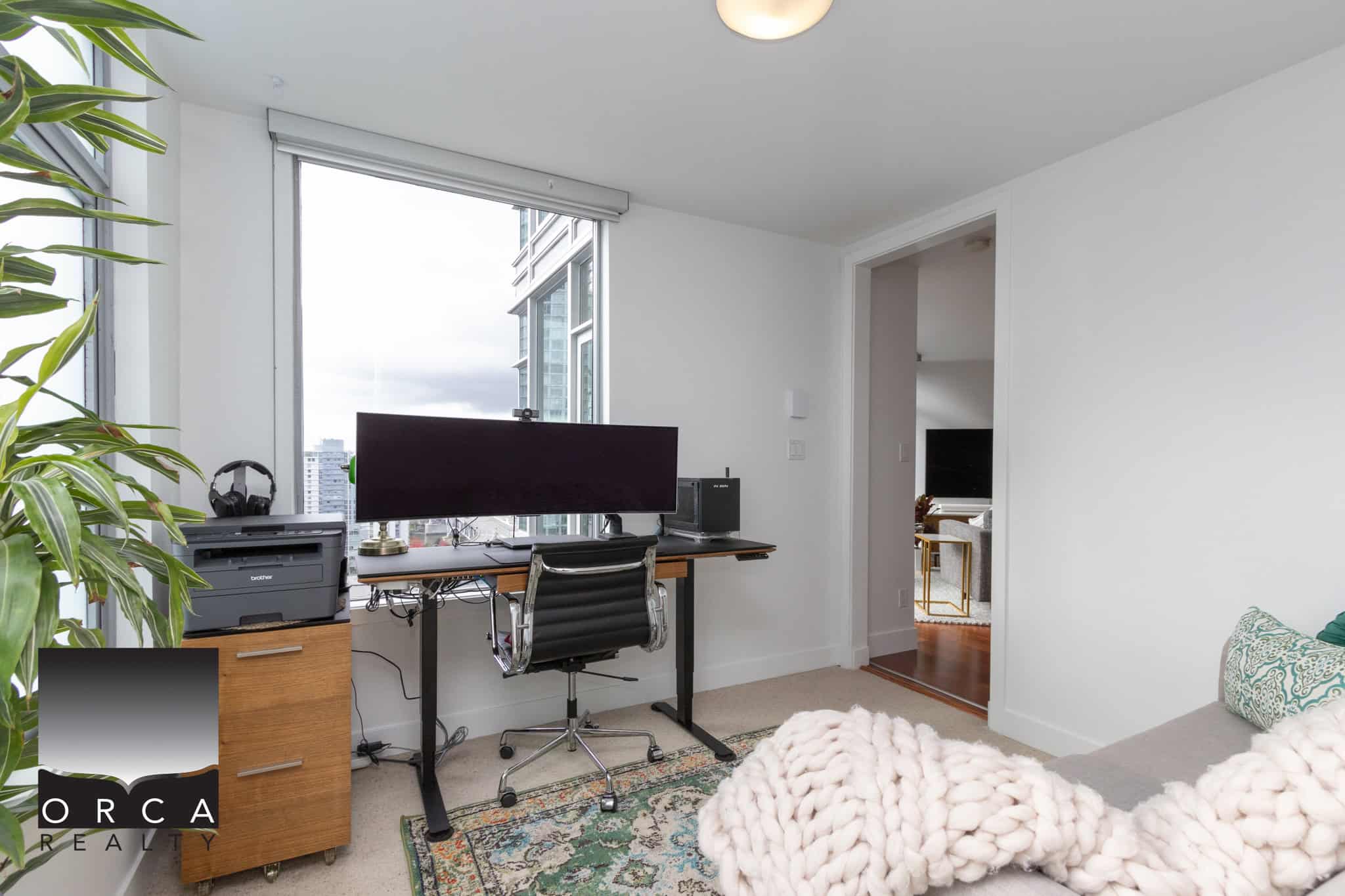 Bright home office space in downtown Vancouver featuring a large window with city views, modern furniture, and a comfortable workspace for real estate professionals.