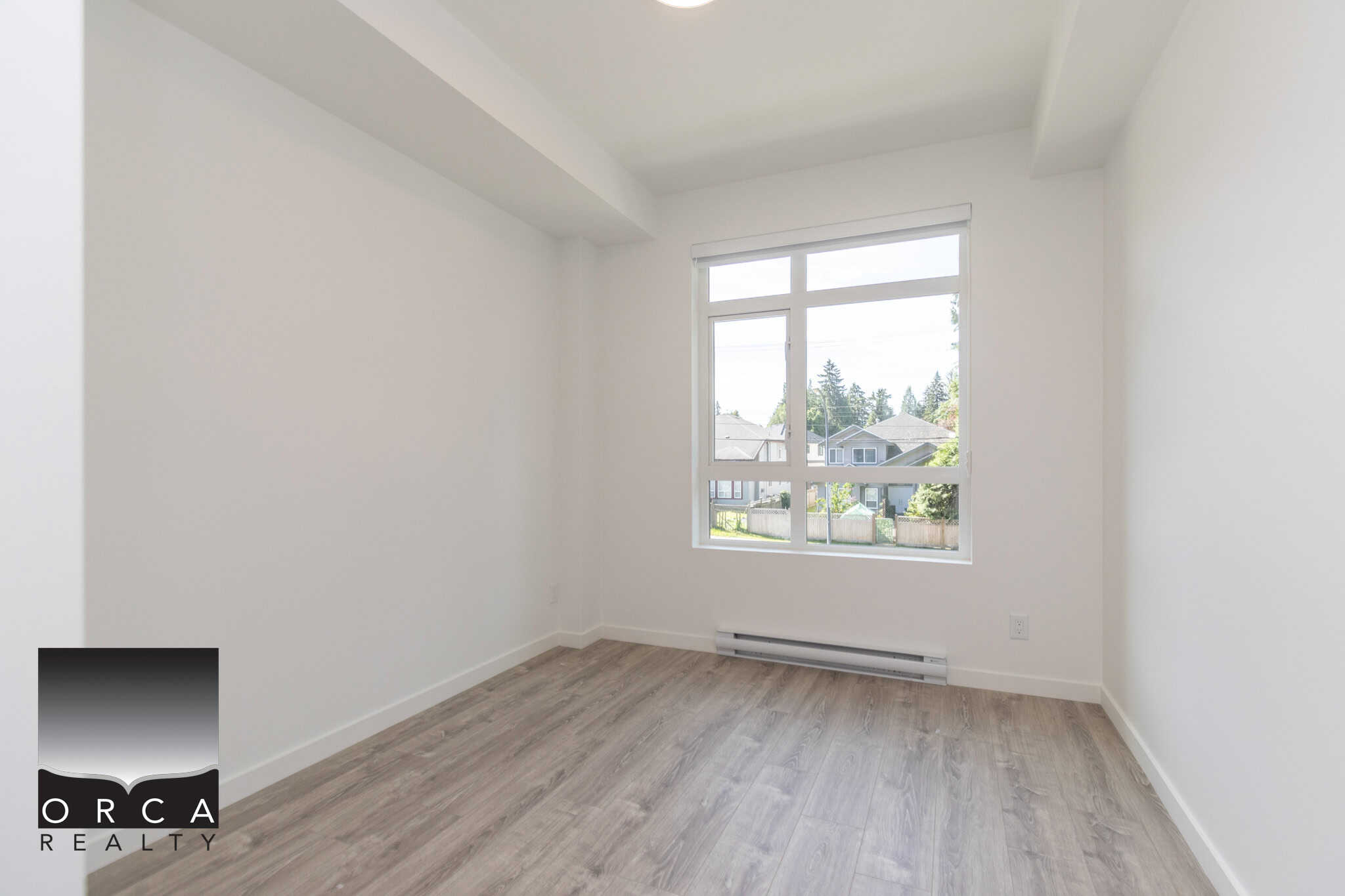 Bright empty bedroom with large window in a modern home, featuring white walls and light wood flooring, ideal for Vancouver area real estate listings.