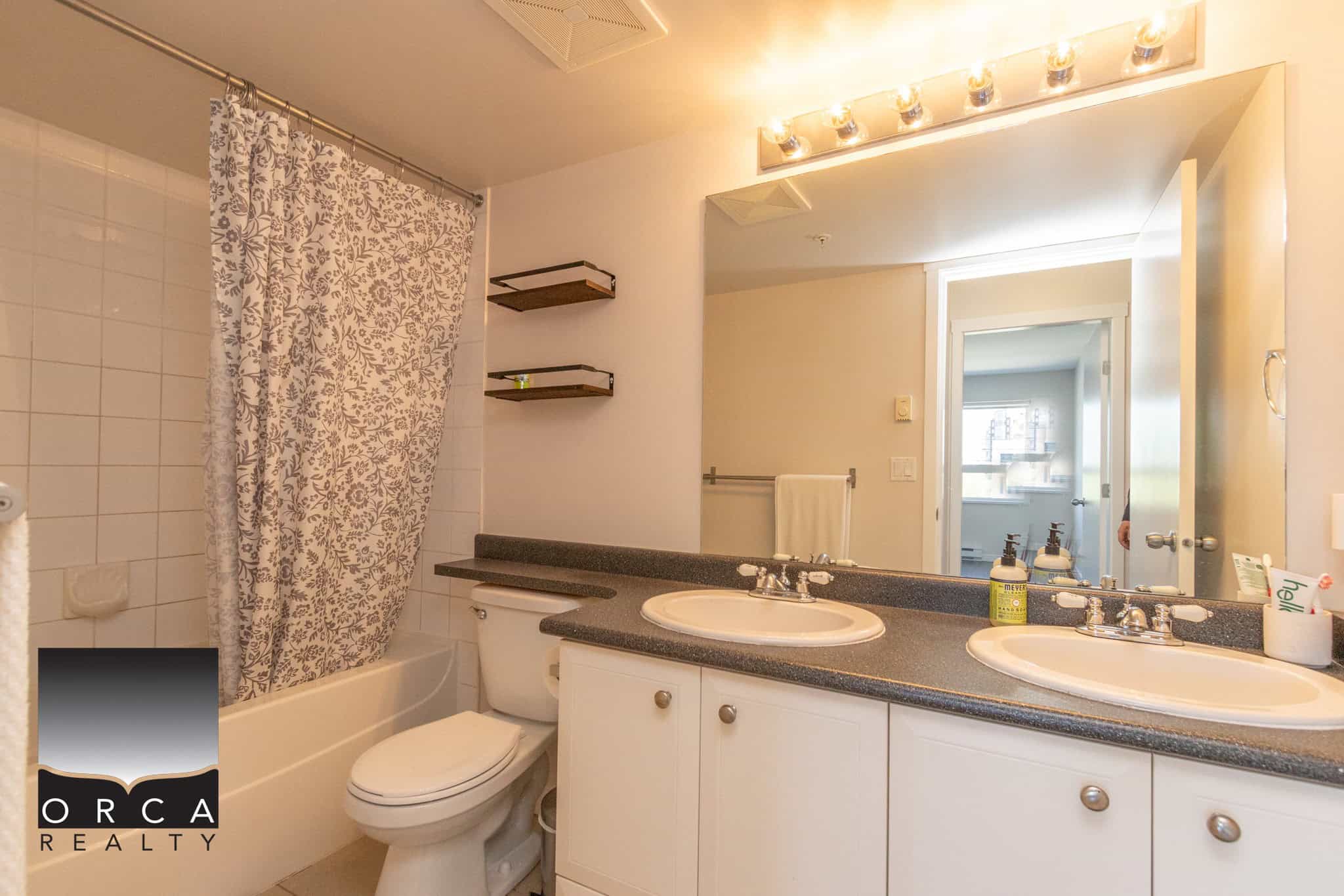 Bright bathroom featuring a double sink vanity with ample storage, a bathtub with a decorative shower curtain, modern fixtures, and a large mirror with lighting, ideal for Vancouver real estate buyers.
