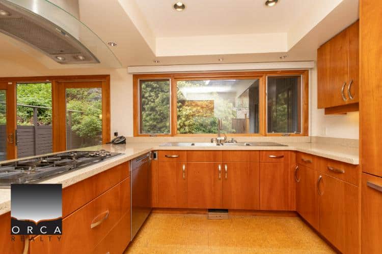 Wooden kitchen cabinetry with large windows showcasing lush greenery, modern appliances, and an inviting atmosphere, ideal for Vancouver real estate listings.