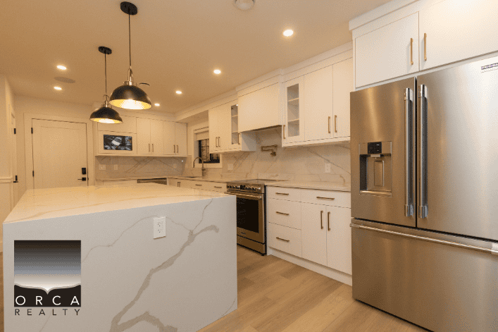 Modern kitchen with white cabinetry, stainless steel appliances, marble countertops, and built-in lighting, perfect for Vancouver real estate listings.