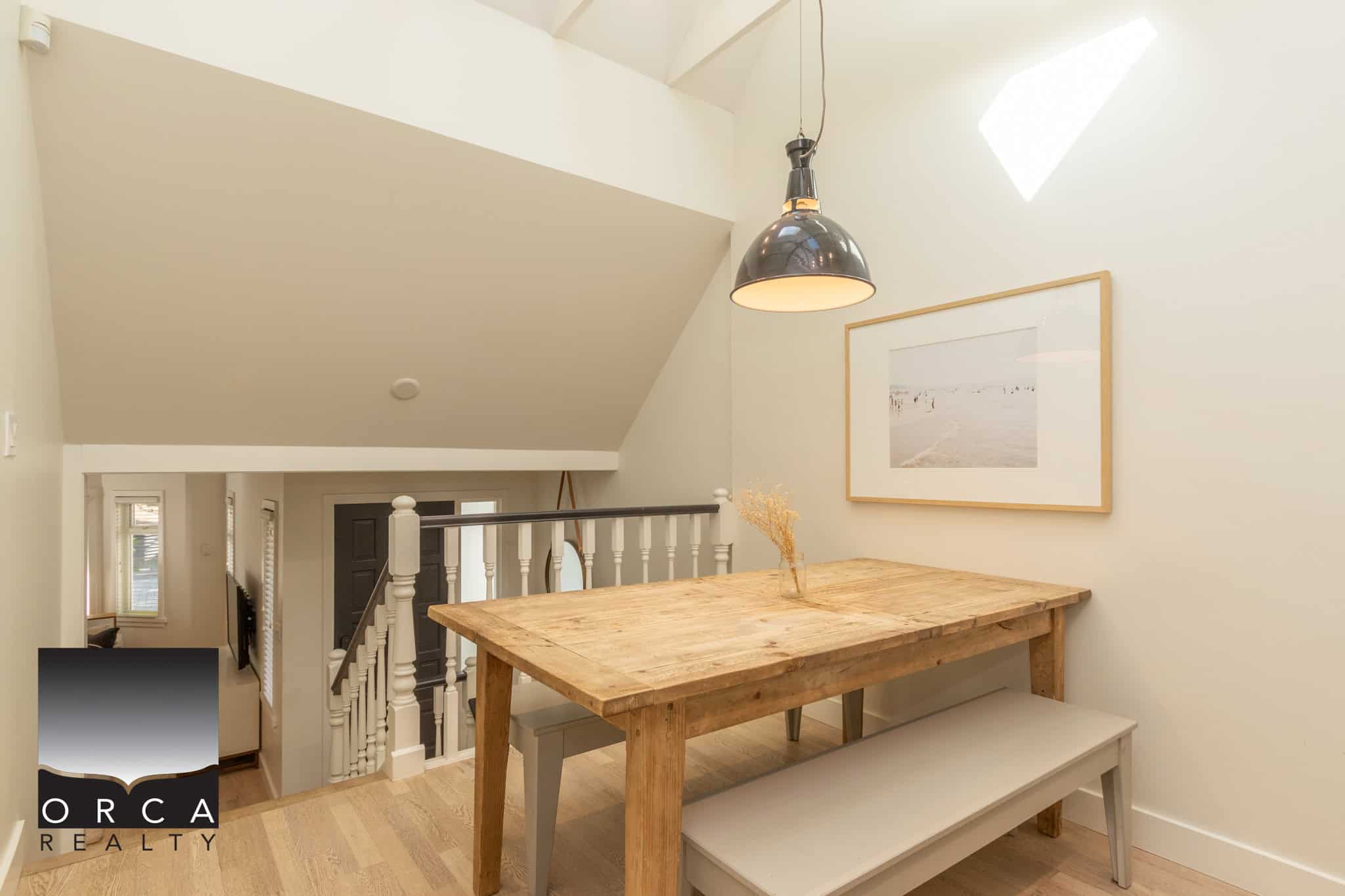 12 Rustic wooden dining table with bench seating in a bright, modern home interior. Natural light from skylight illuminates the space, with minimalist decor and neutral tones enhancing the airy feel.