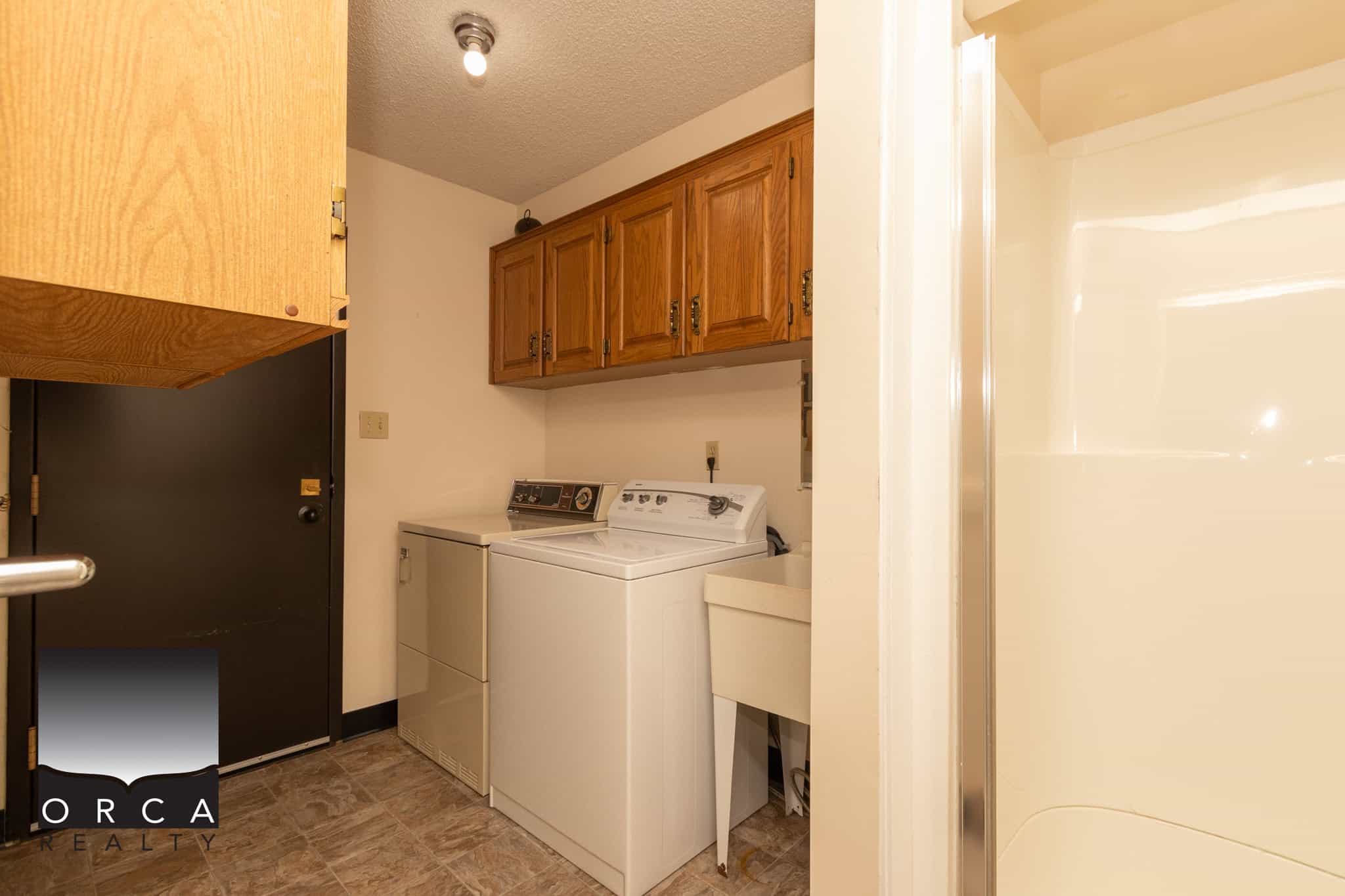Apartment laundry room with washer and dryer in Vancouver, BC, residential laundry area, household appliances, utility space, wooden cabinets, clean and functional laundry setup, home essentials, real estate property, Orca Realty Inc.