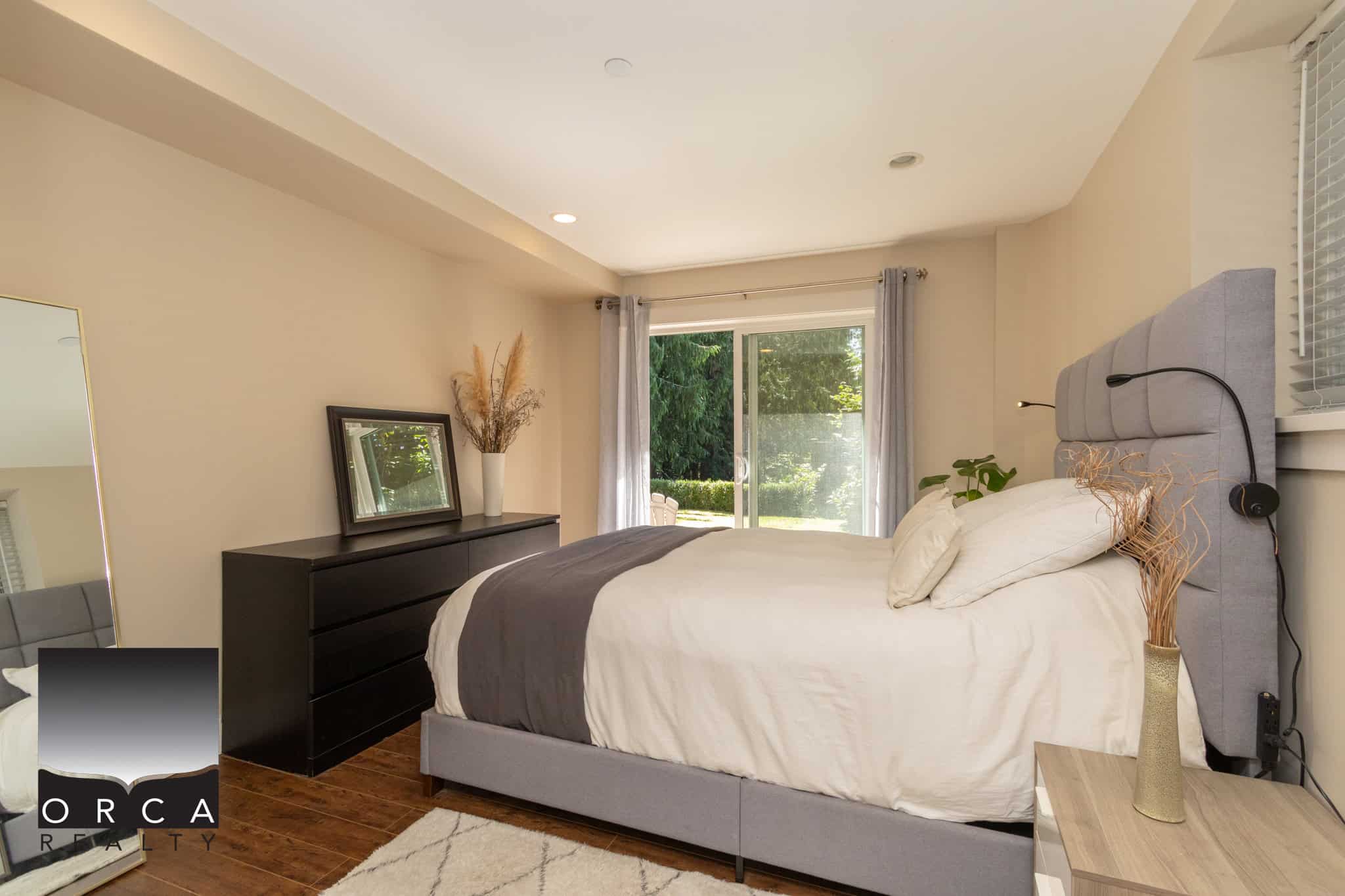 Bright modern bedroom with large window and sliding glass door, cozy bed with headboard, neutral decor, and abundant natural light, perfect for Vancouver Island homes.