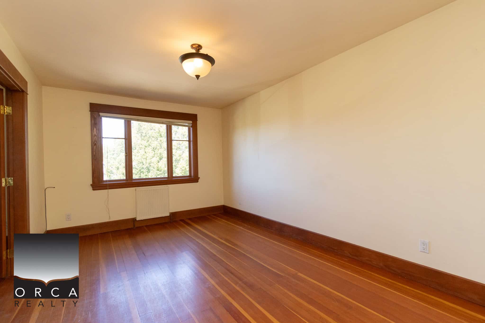 Bright empty living room with hardwood floors, large window, and natural wood trim, ideal for Vancouver homebuyers seeking cozy and stylish interior spaces.