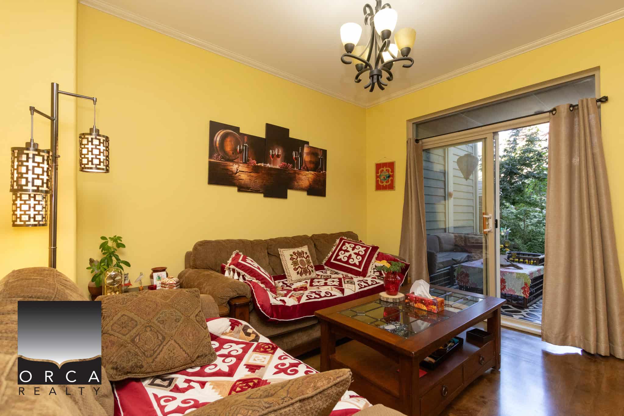 12 Cozy living room with yellow walls, comfortable seating, and vibrant decor, featuring a sliding glass door to a balcony with lush greenery, perfect for homebuyers seeking a warm, inviting Canadian residence.