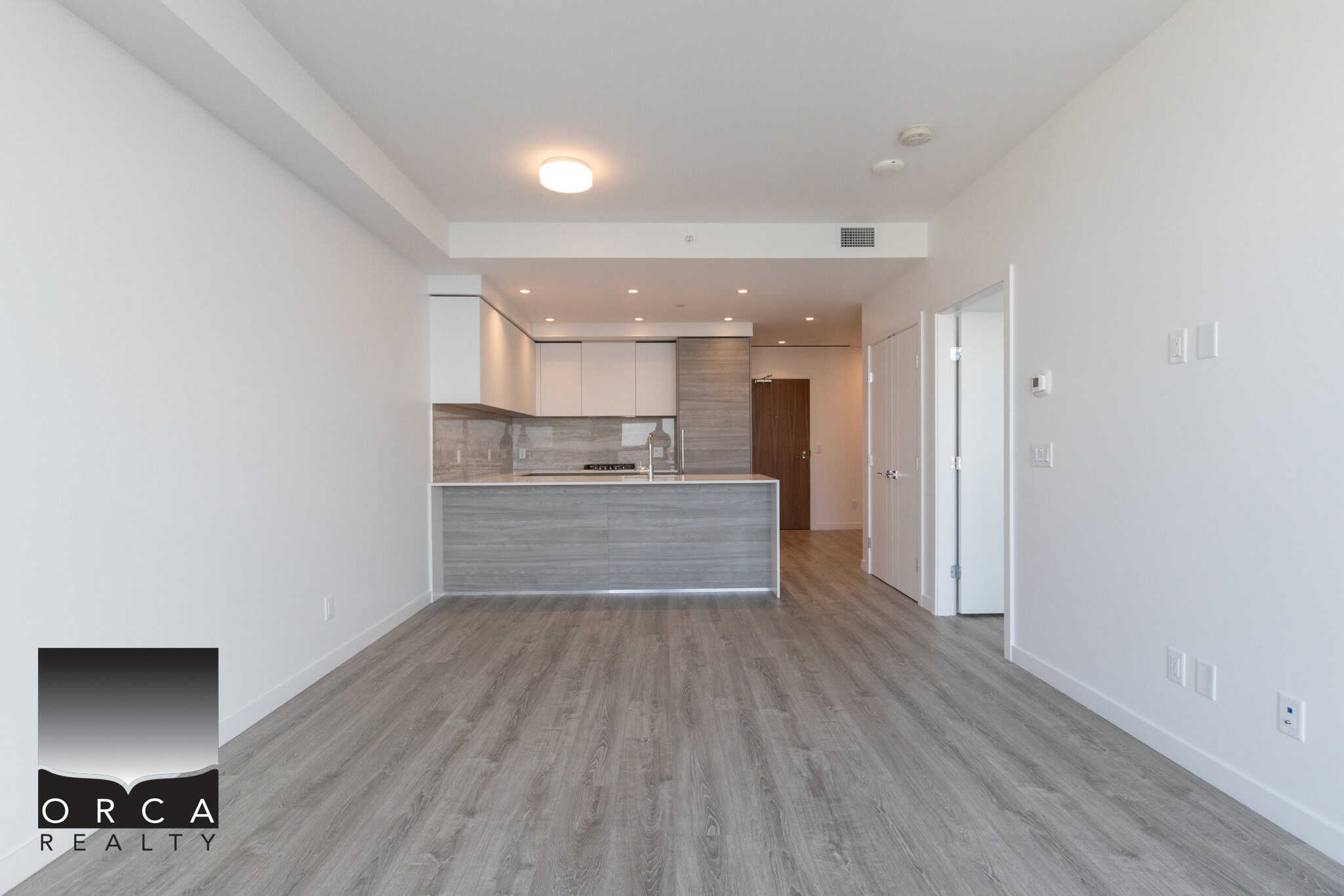 12 Modern vacant apartment interior with open-concept kitchen, light wood flooring, white walls, contemporary cabinetry, ideal for Vancouver-area real estate listings.
