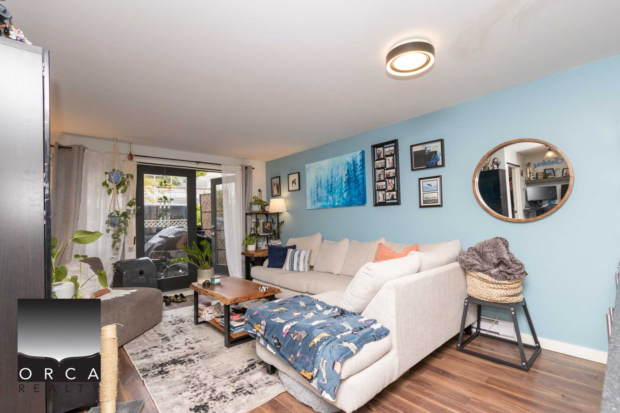 Bright living room with cozy sectional sofa, stylish wall art, and ample natural light from sliding glass doors, perfect for Vancouver Island real estate living.