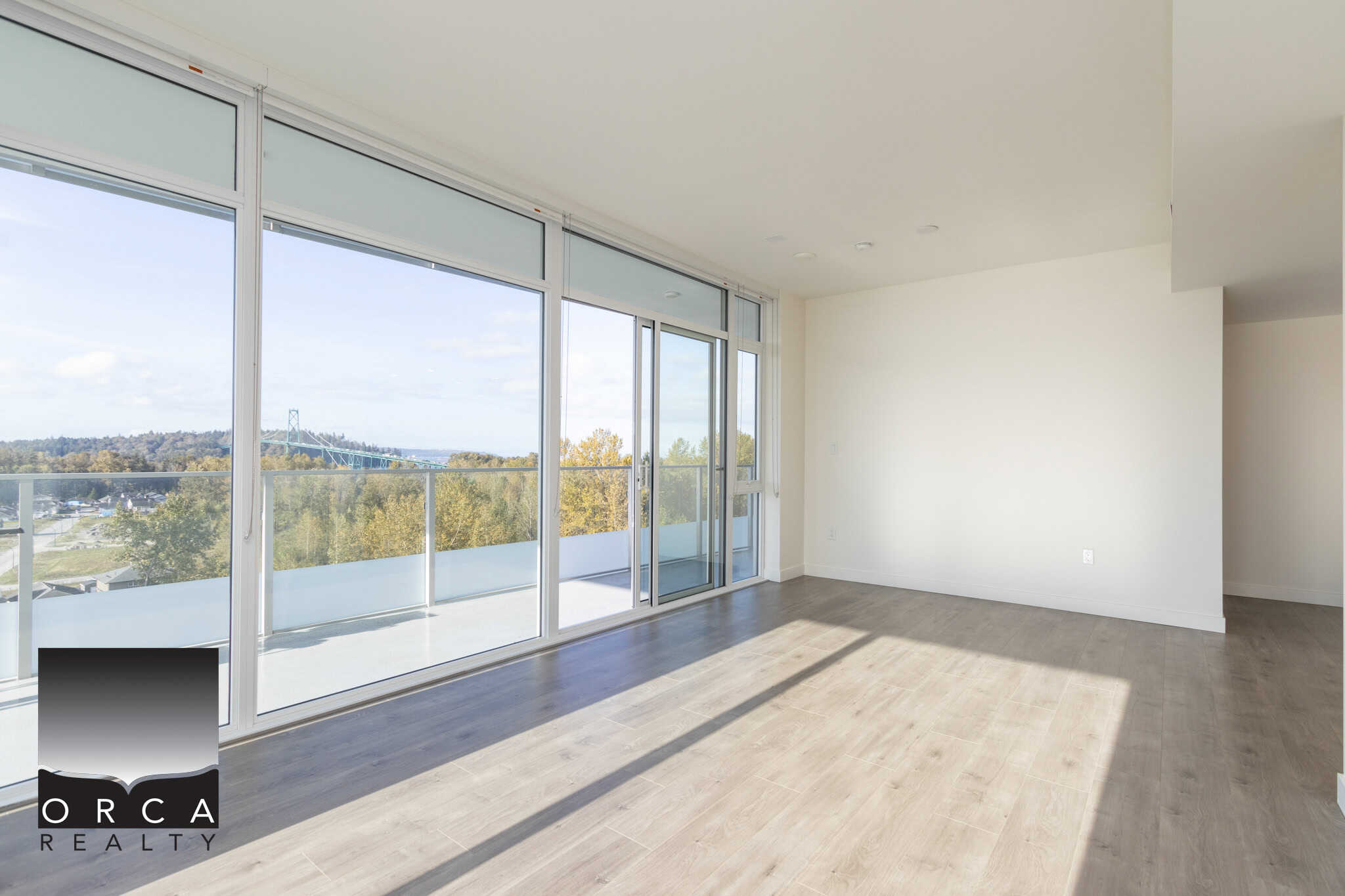 Bright living room with large floor-to-ceiling windows offering stunning views and natural light, modern flooring, and access to a balcony, perfect for Vancouver area real estate.