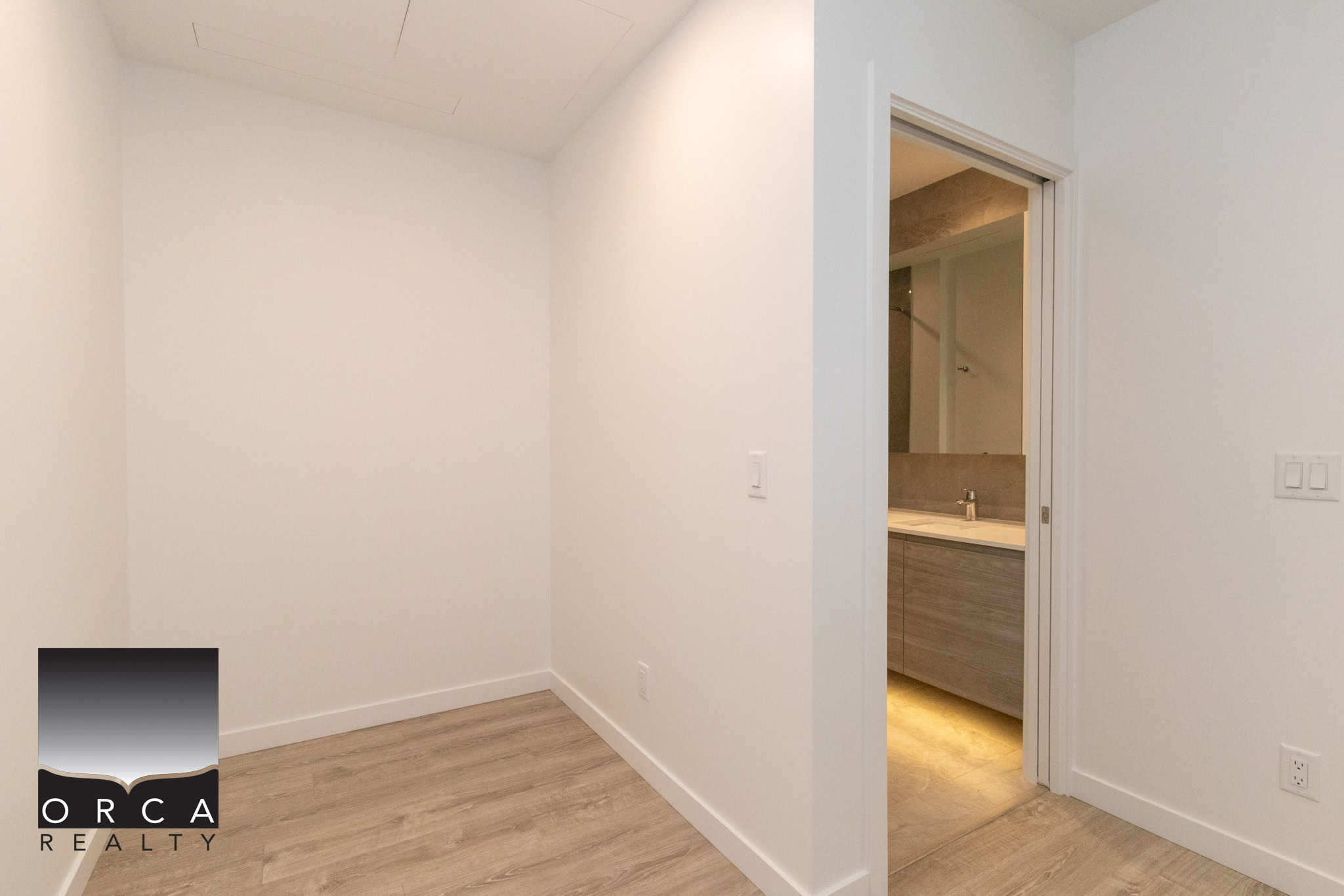 13 Bright modern interior space with white walls, light wood flooring, and an open doorway leading to a contemporary bathroom; ideal for Vancouver real estate listings.