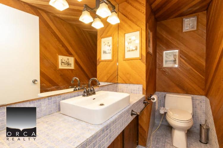 Modern rustic bathroom with wood-paneled walls, white sink, tiled countertop, and toilet, showcasing home renovation and real estate features in BC.