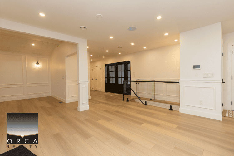 Interior of modern residential property showcasing spacious living area with hardwood flooring, recessed lighting, white walls, and black door accents in Vancouver, BC.