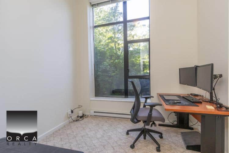 Modern home office with dual monitors, ergonomic chair, and large window for natural light, ideal for remote work or study. Perfect Vancouver area real estate workspace.