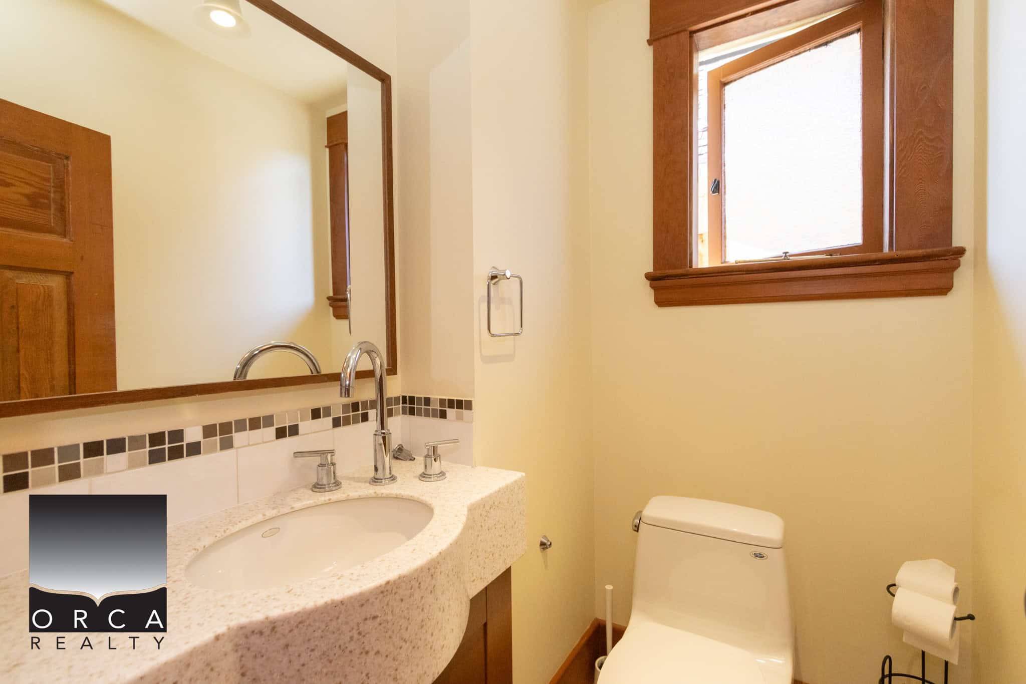 Bright bathroom with a natural wood-framed window, modern fixtures, and a granite countertop sink, ideal for Vancouver Island homes in a cozy, inviting setting.