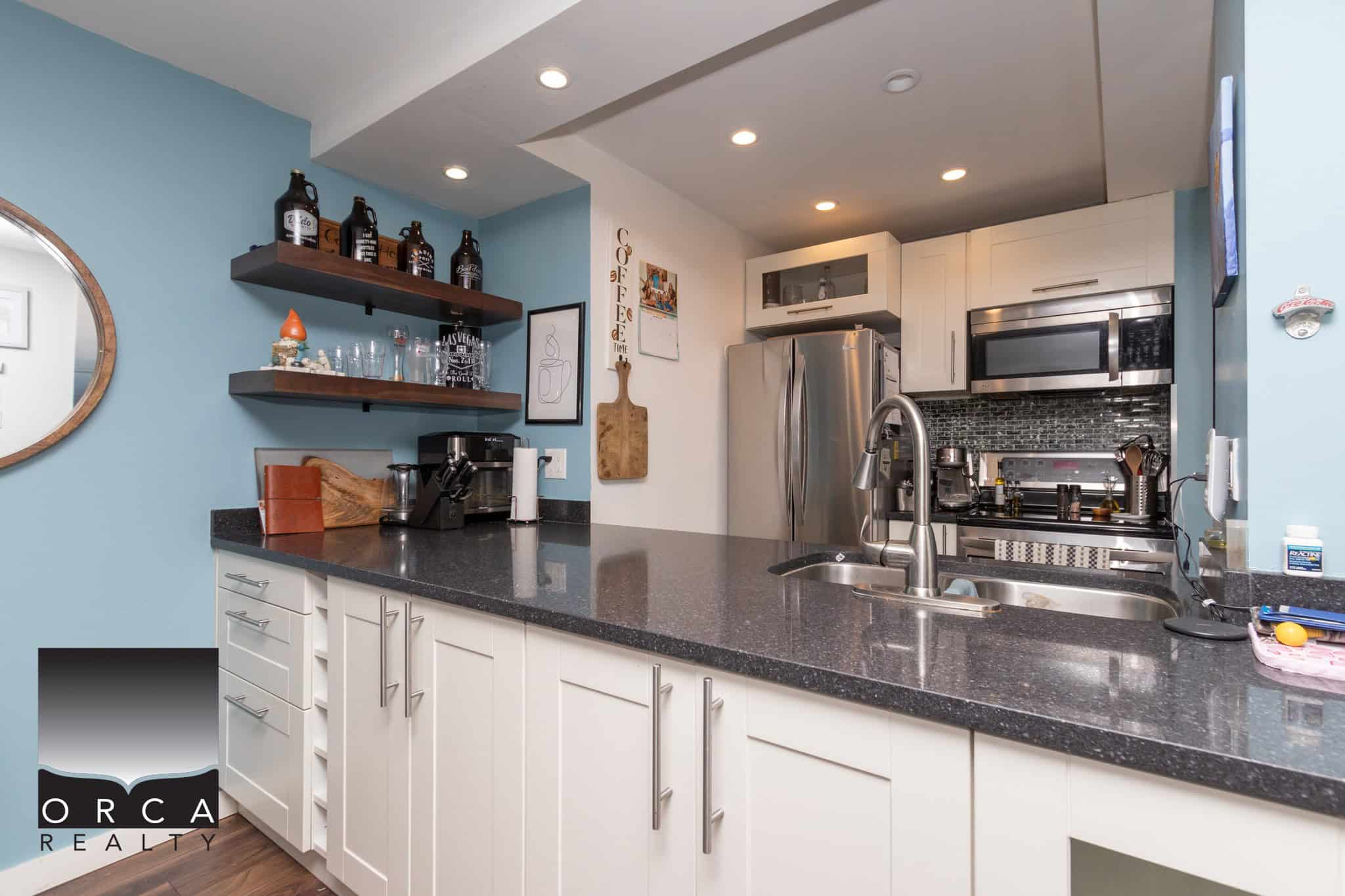 Bright modern kitchen with white cabinetry, black granite countertops, stainless steel appliances, blue accent wall, and open shelving, perfect for home cooking and entertaining.