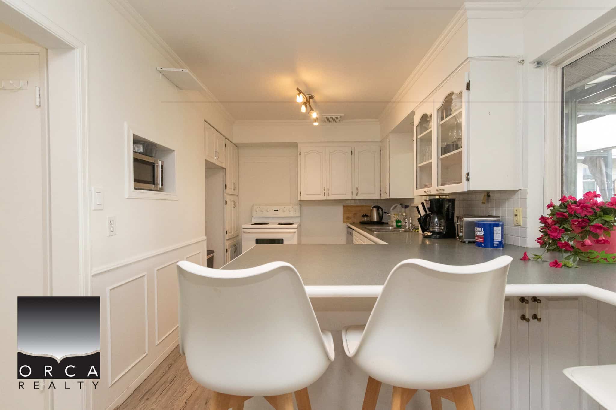 14 Bright white kitchen with counter seating, modern appliances, and large window, ideal for Vancouver Island homebuyers seeking coastal real estate.