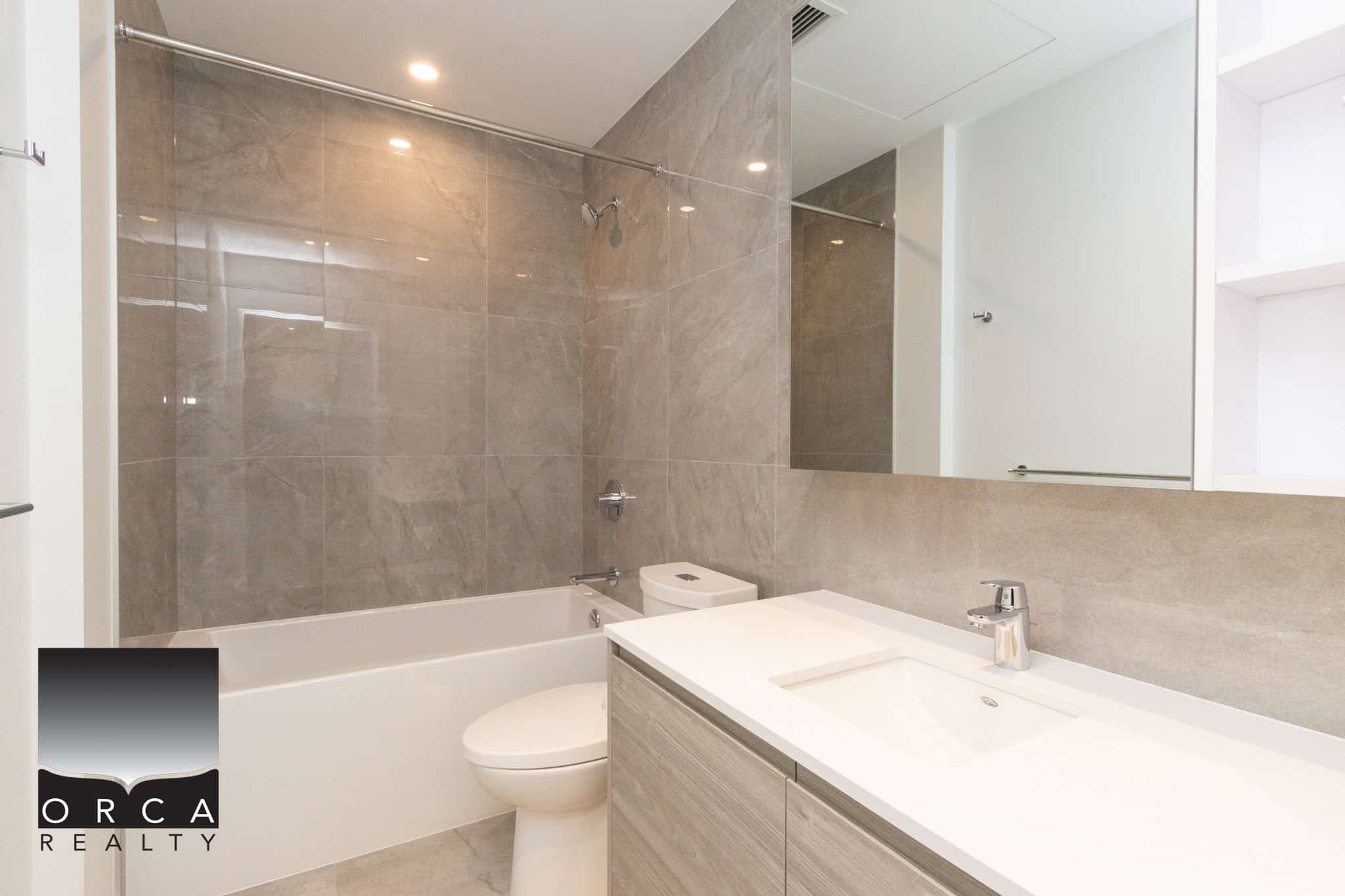 14 Modern bathroom with beige tile walls, white bathtub, sleek vanity with integrated sink, and contemporary fixtures, showcasing upscale real estate features by Orca Realty Inc.