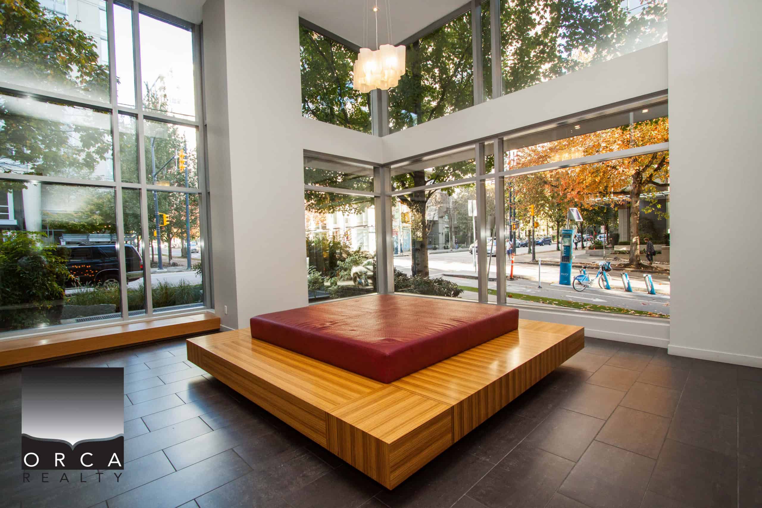 Modern real estate office interior with large floor-to-ceiling windows showcasing city street views, perfect for client consultations and property showings in Vancouver's downtown core.
