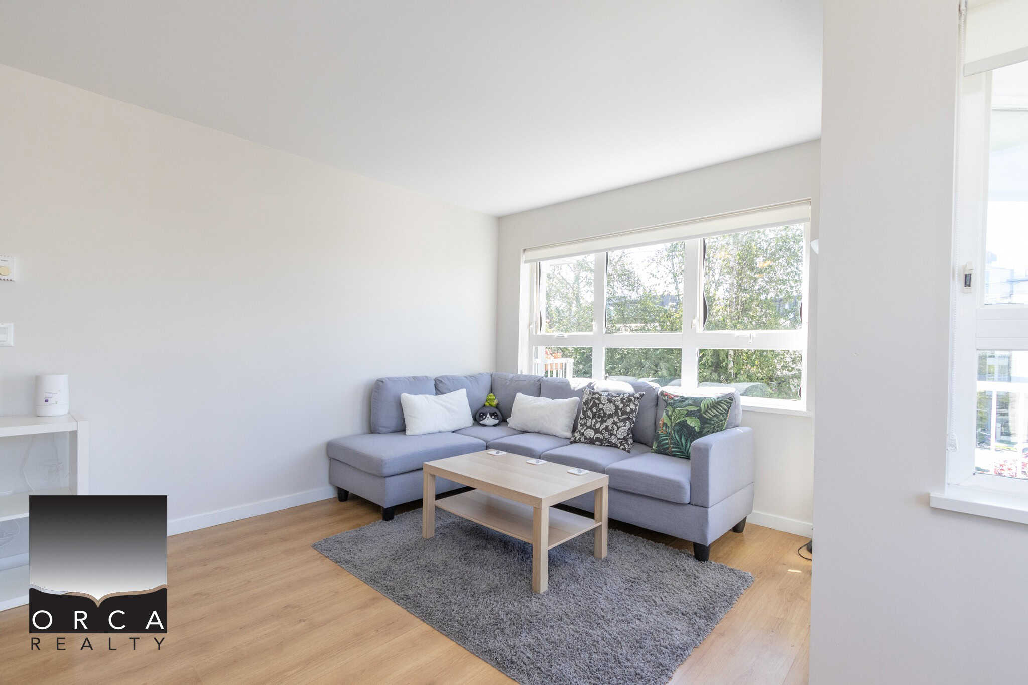 Bright living room with large windows, modern grey sofa, and cozy decor, showcasing a stylish and inviting space perfect for relaxed home living in Vancouver.
