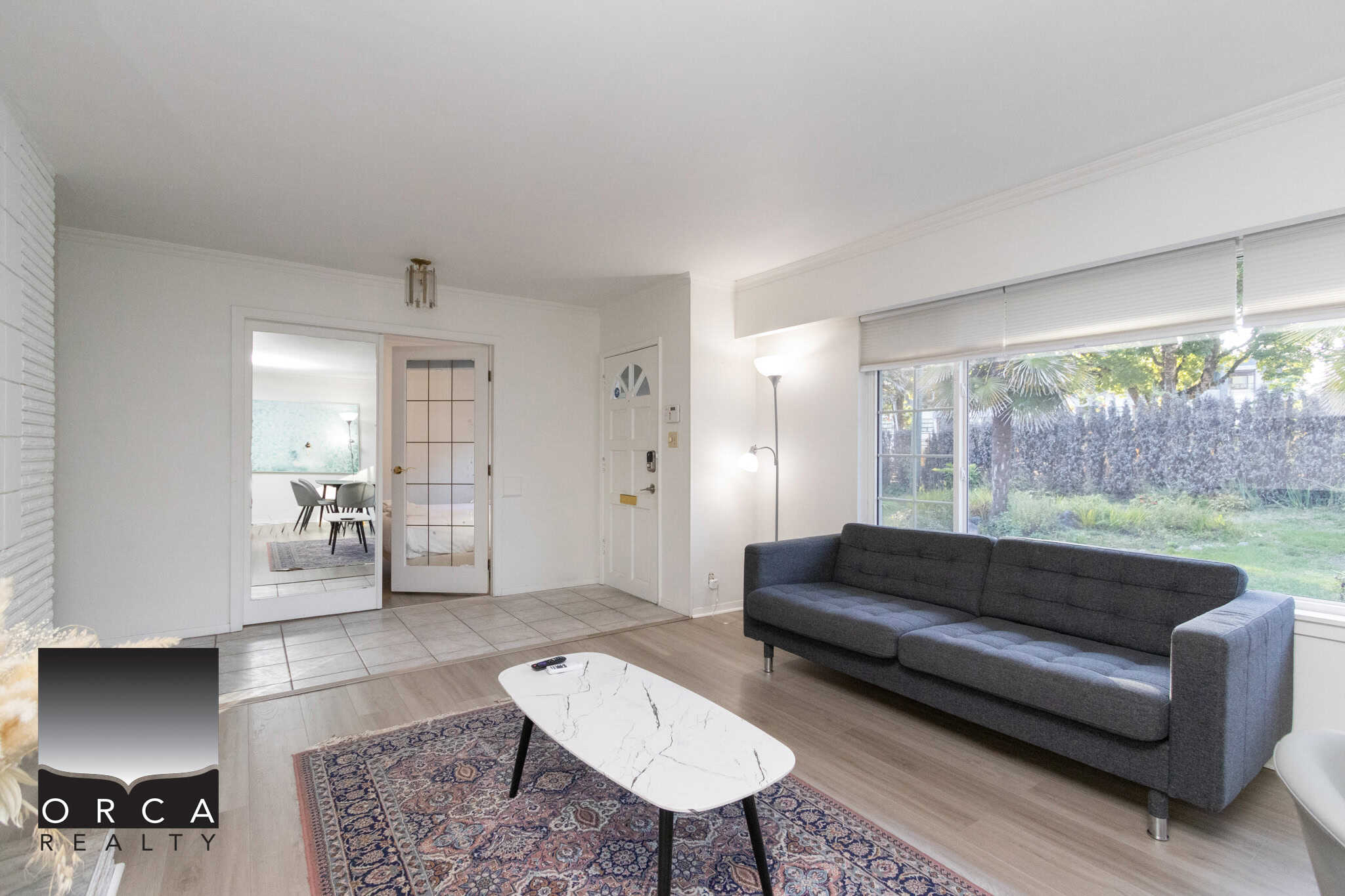 15 Cozy living room with large window views, modern furniture, and bright natural light, showcasing inviting residential space for sale or rent by Orca Realty Inc.