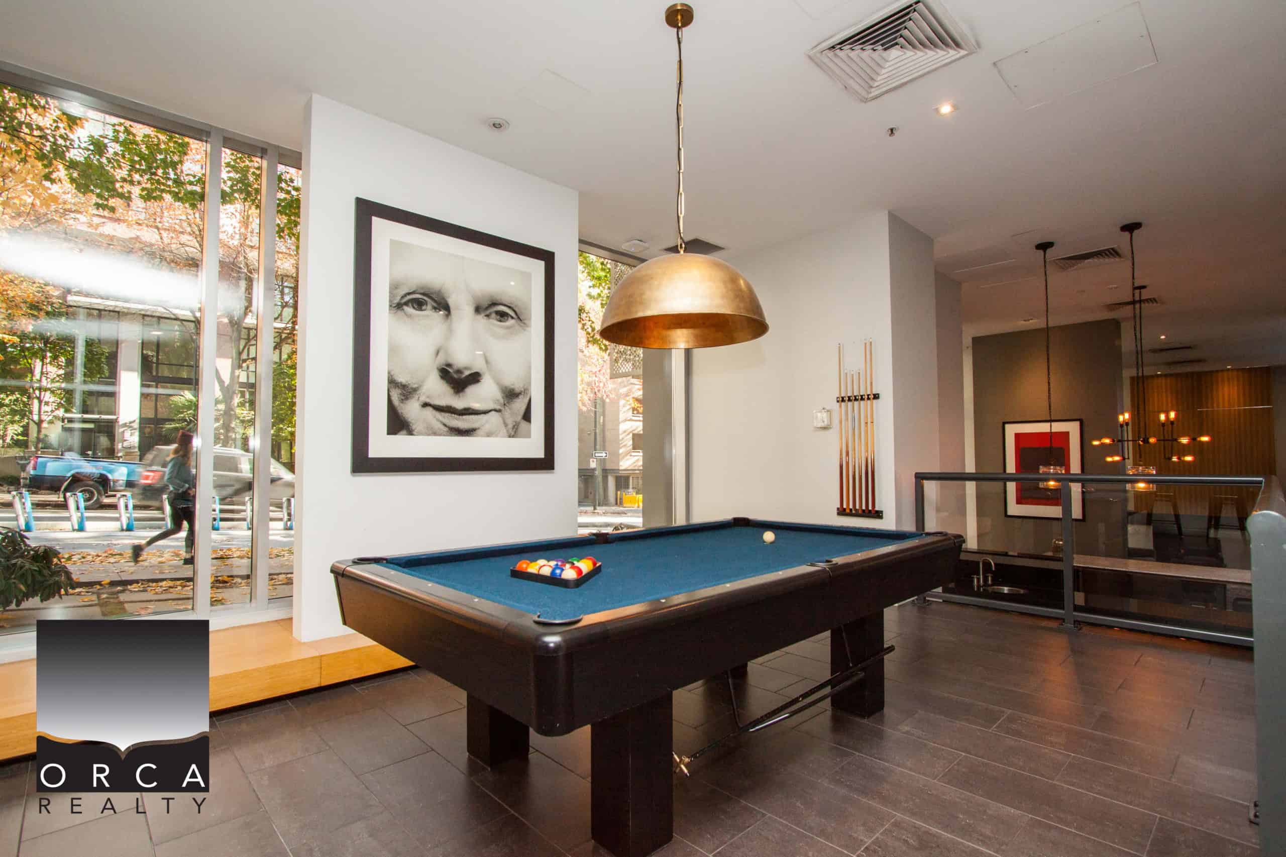Contemporary indoor recreation area with a pool table, stylish pendant lighting, and modern artwork, ideal for relaxing or entertaining clients in a professional real estate office.