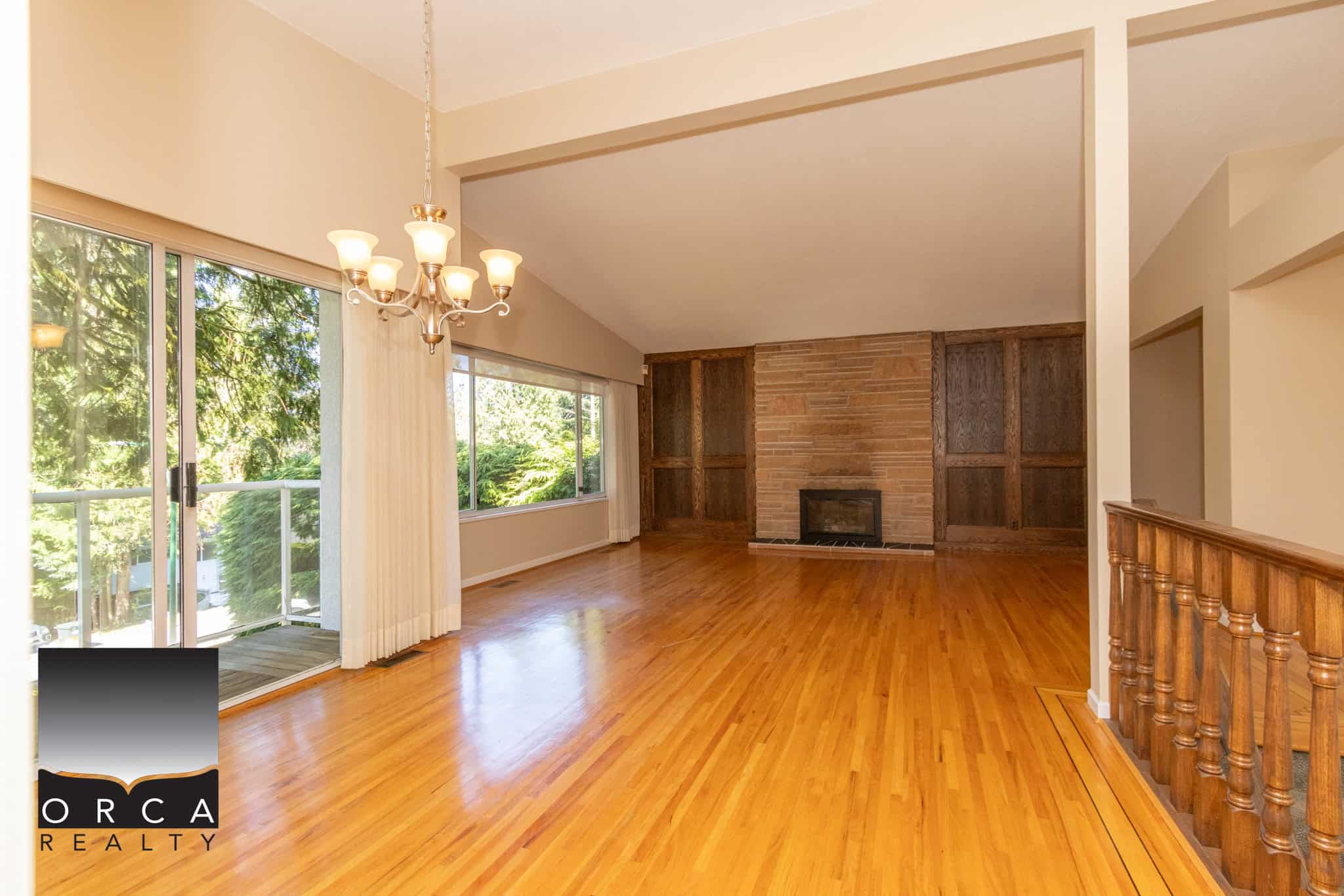 Spacious living room with large windows, hardwood flooring, and a cozy brick fireplace, ideal for family gatherings and relaxing in a beautiful home listed by Orca Realty Inc.