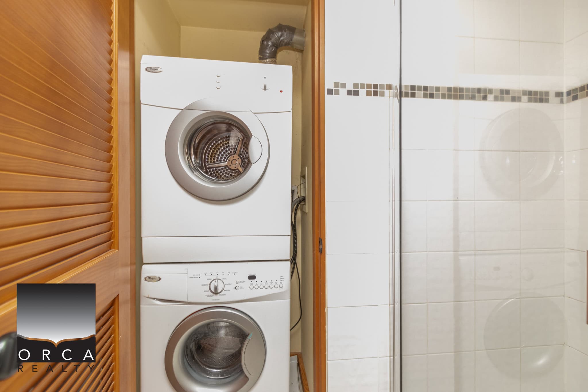 Stacked front load washer and dryer in laundry area with white tile walls, perfect for Ottawa real estate listings.