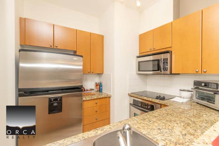 Modern stainless steel refrigerator and microwave in a contemporary kitchen with granite countertops and wooden cabinetry.