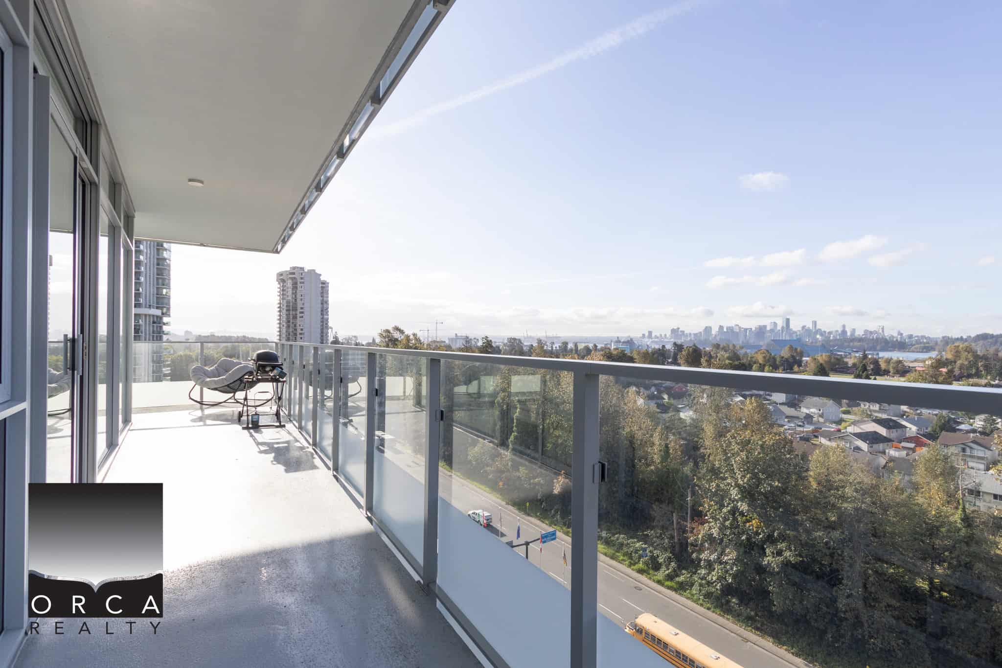 Spacious balcony with modern glass railing offering panoramic city and river views in a high-rise condo in Vancouver, BC. Perfect for relaxing and entertaining while enjoying the outdoors.