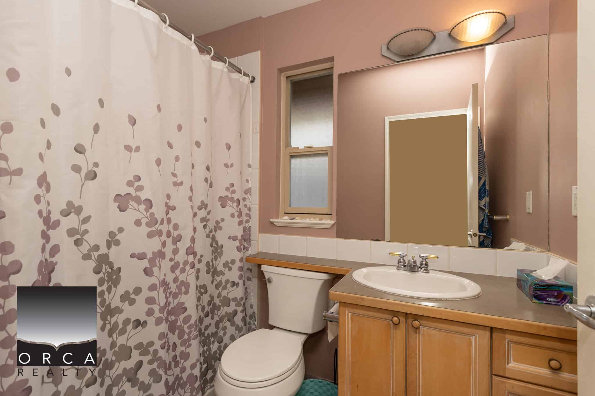 16 Bright bathroom with painted pink walls, shower curtain, white toilet, wooden vanity, large mirror, and small window, ideal for Vancouver home listings - Orca Realty Inc.