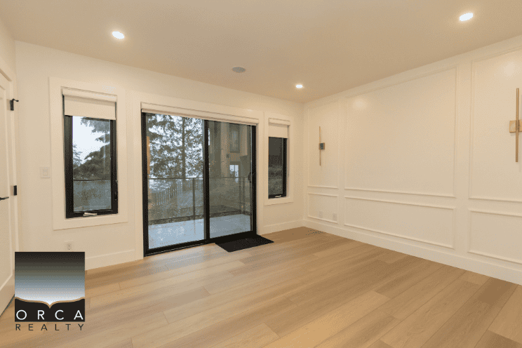 Modern living room with large sliding glass doors and windows, hardwood floors, and white wall paneling, ideal for Vancouver area homes.