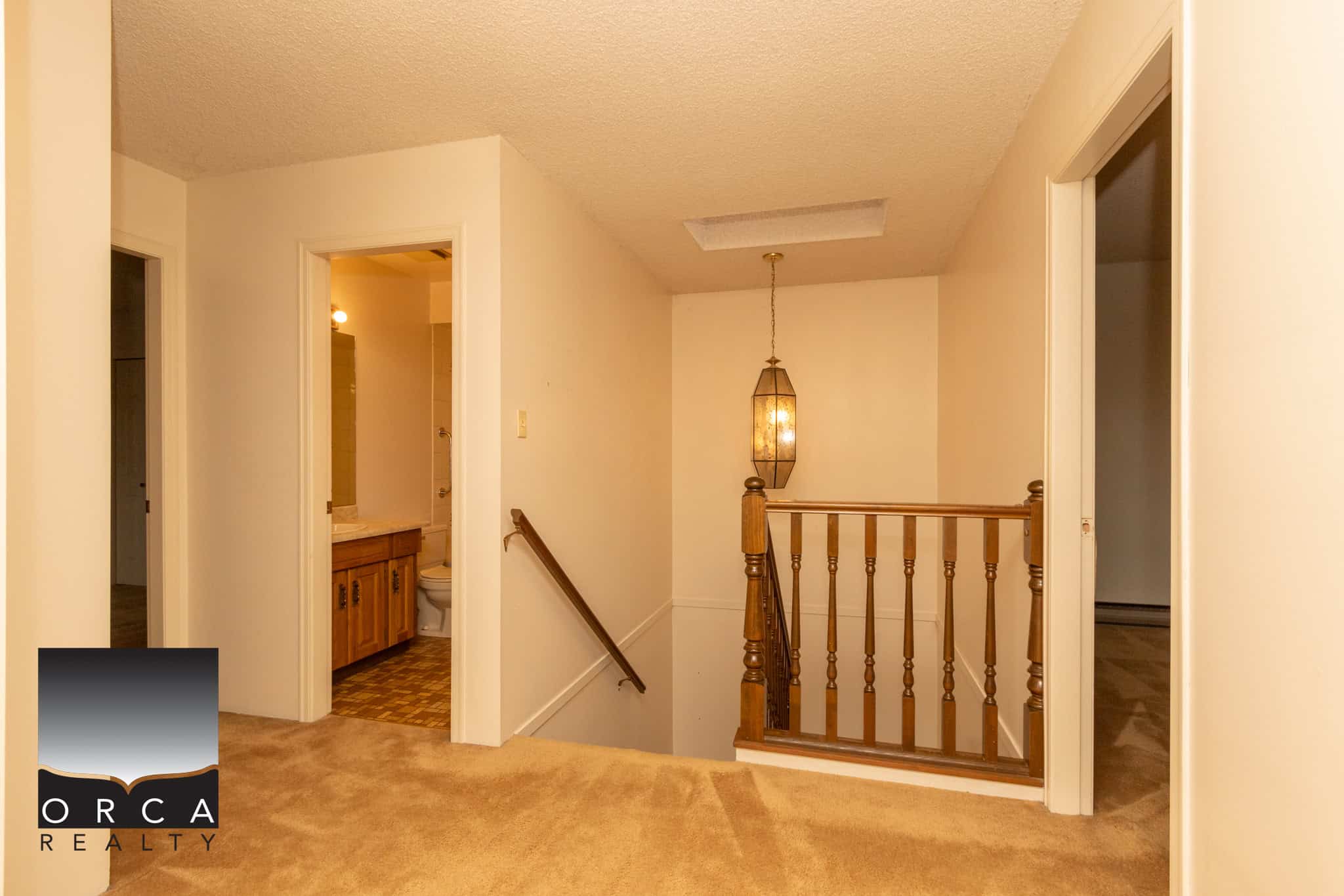 Bright upstairs hallway with beige carpet, natural light, and wooden handrail leading to bedrooms and bathroom at Orca Realty Inc.