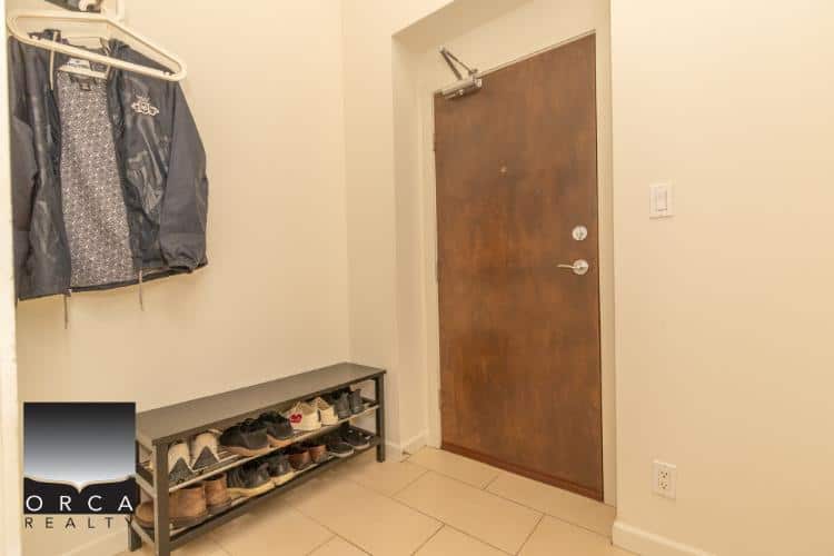 Spacious apartment entryway with shoe rack and coat hanging area, features a wooden door, perfect for Vancouver real estate listings.