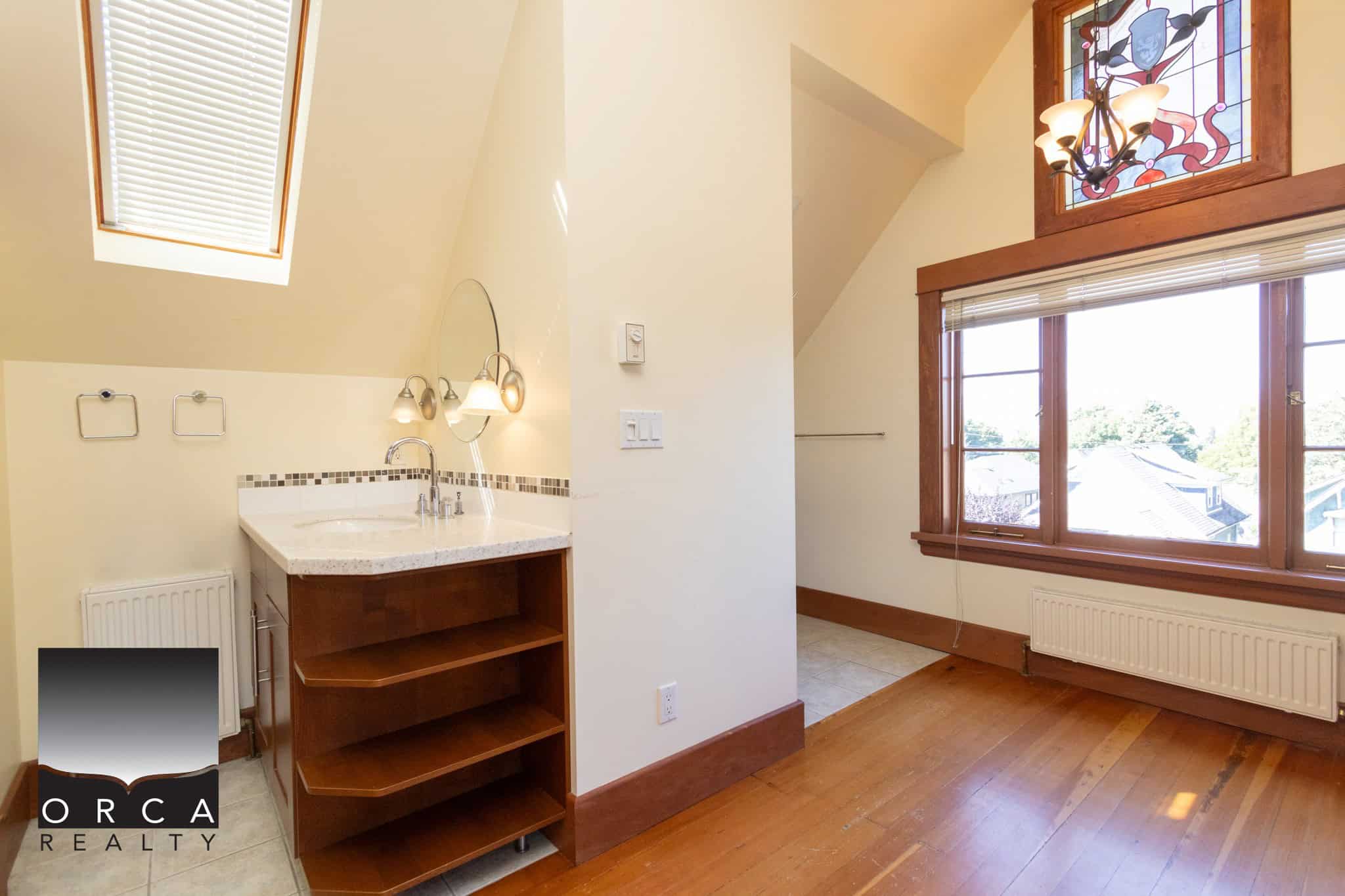 Elegant bathroom with large windows, skylight, and stained glass accent, featuring hardwood floors, natural light, and modern fixtures; ideal for a stylish Vancouver-style home.