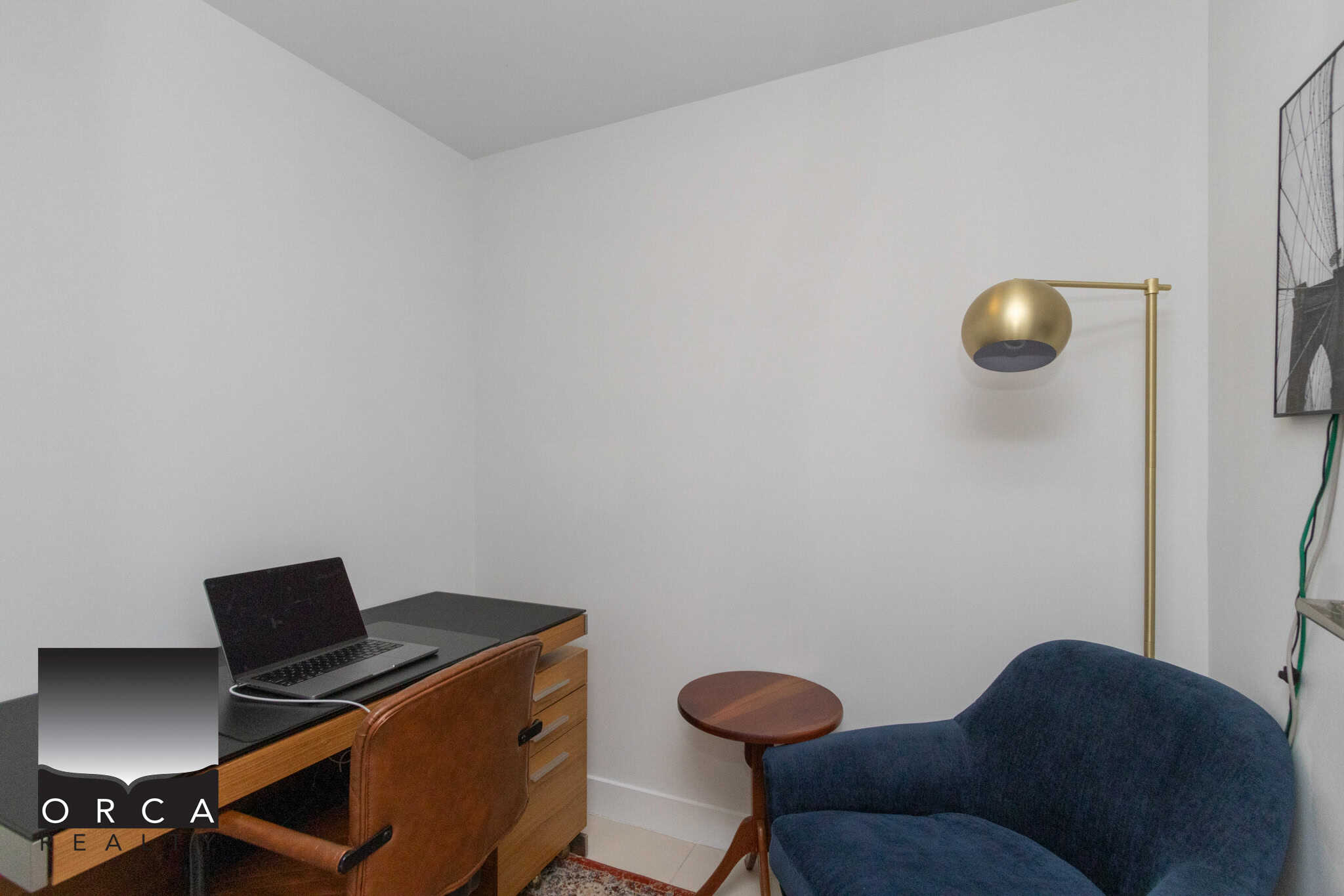 Cozy home office with white walls, a laptop on a wooden desk, a comfortable blue armchair, and modern gold floor lamp. Perfect for remote work or study in a Vancouver or British Columbia home.