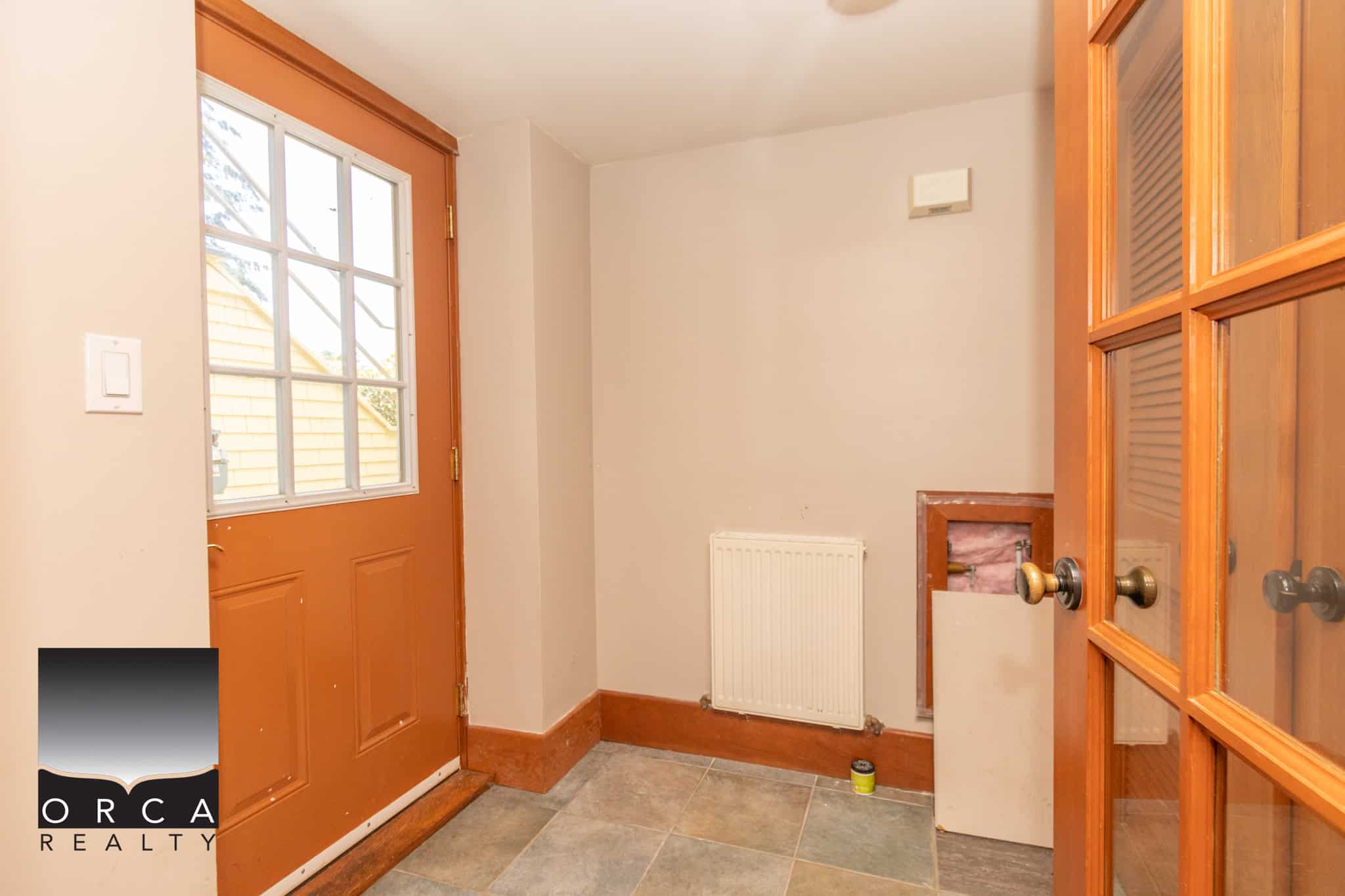 Cozy entrance hall in a Canadian home with a wooden door, tiled flooring, and a glass-paneled inner door, featuring natural light and a radiator for comfort, ideal for real estate listings.