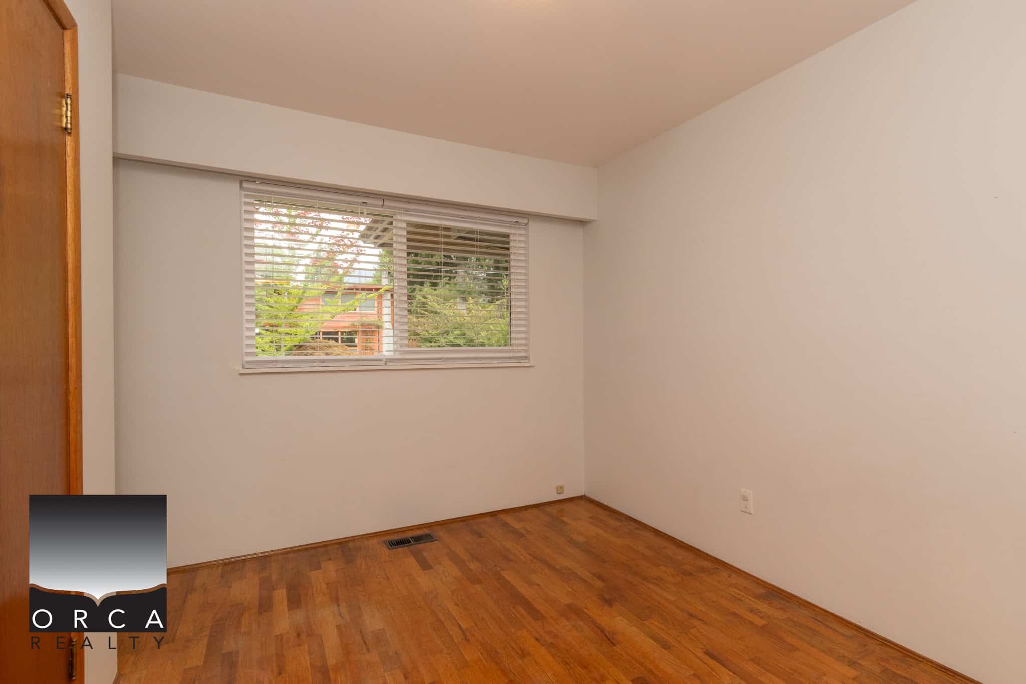 18 Bright empty bedroom with hardwood flooring and a large window showcasing a green backyard view, ideal for Vancouver Island home buyers looking for comfortable real estate options.
