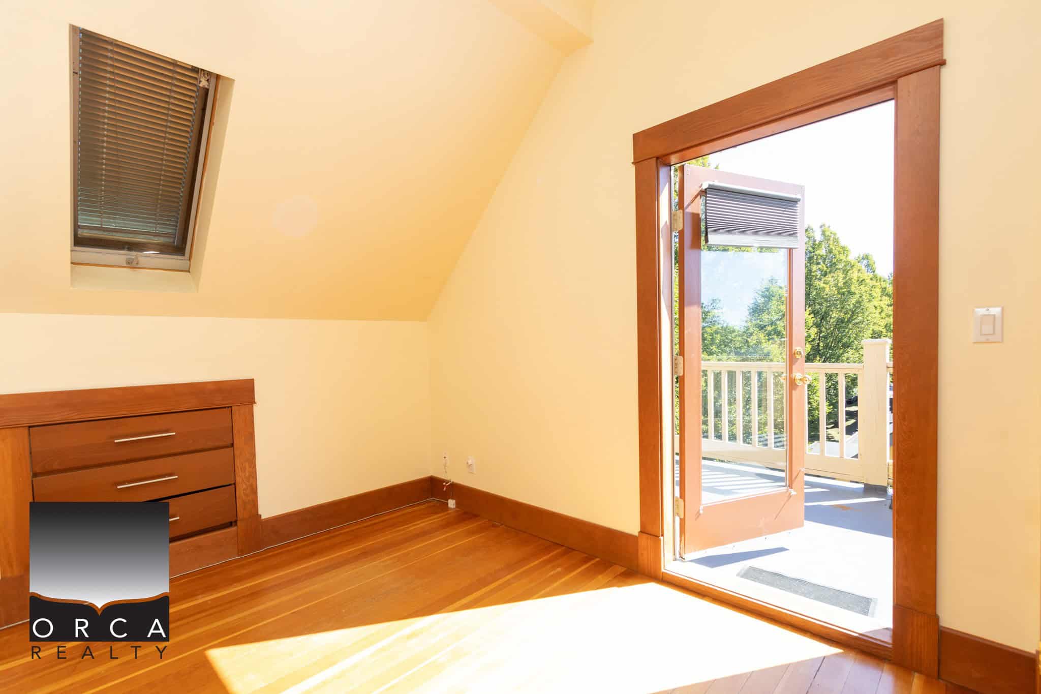 Bright cozy attic bedroom with large skylight and balcony door, natural sunlight, wooden trim, hardwood floors, perfect for Vancouver Island homes.