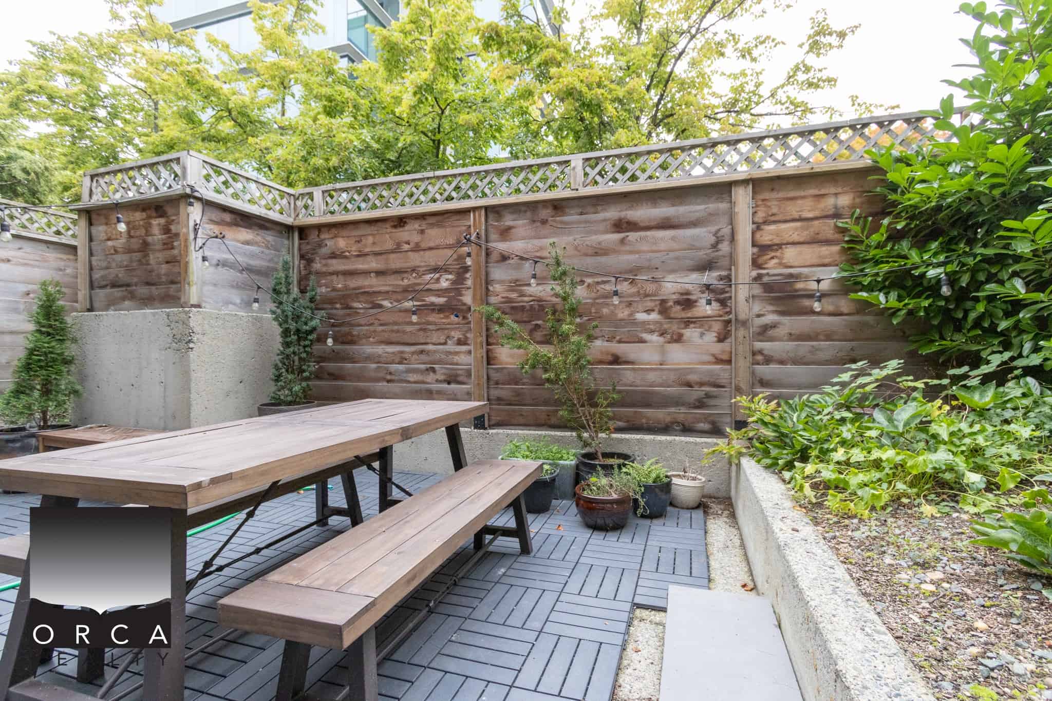 Handyman outdoor patio with wooden fencing, string lights, planting pots, and wooden picnic table, perfect for Vancouver real estate and property management.