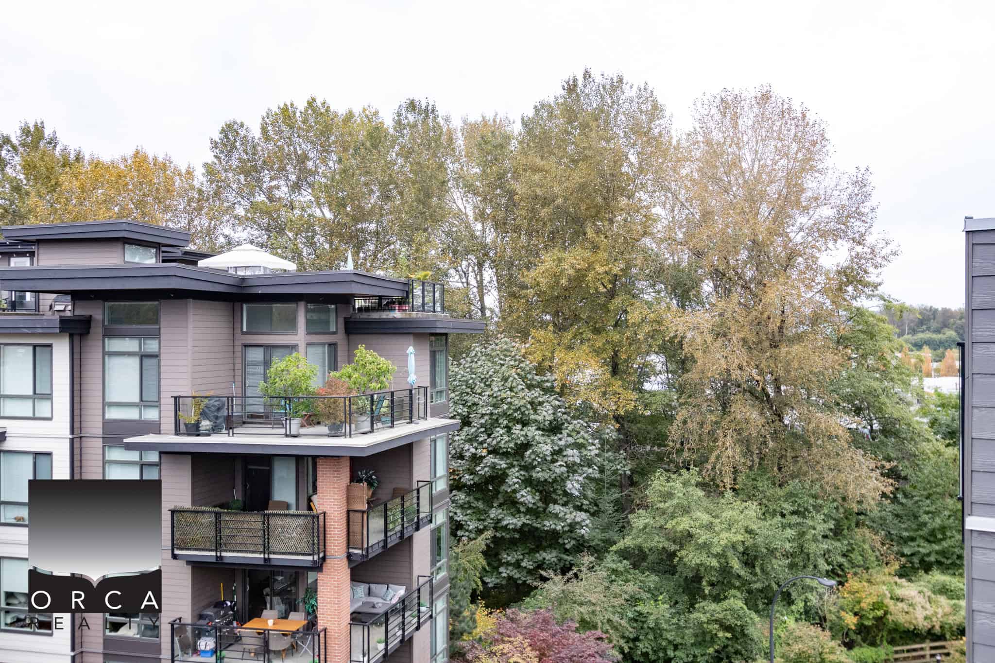 Modern multi-unit residential condo building with outdoor balconies surrounded by lush autumn trees in Vancouver, BC, Canada.