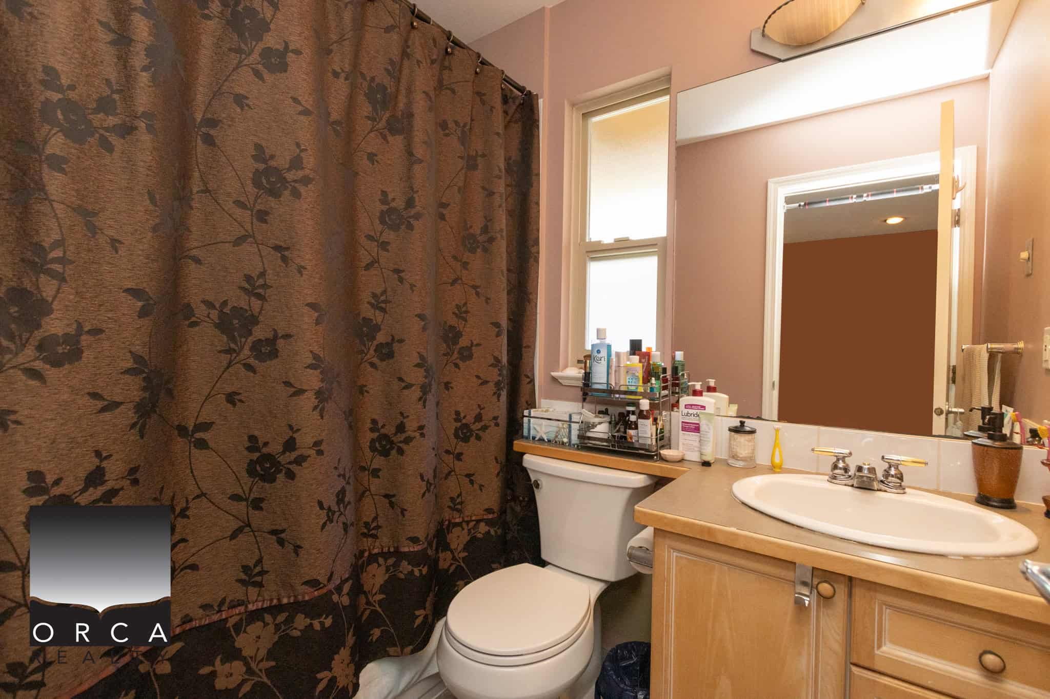 18 Bright bathroom with a beige vanity, oval sink, and a window above the toilet providing natural light, featuring personal care products and a decorative mirror for a cozy home feel.