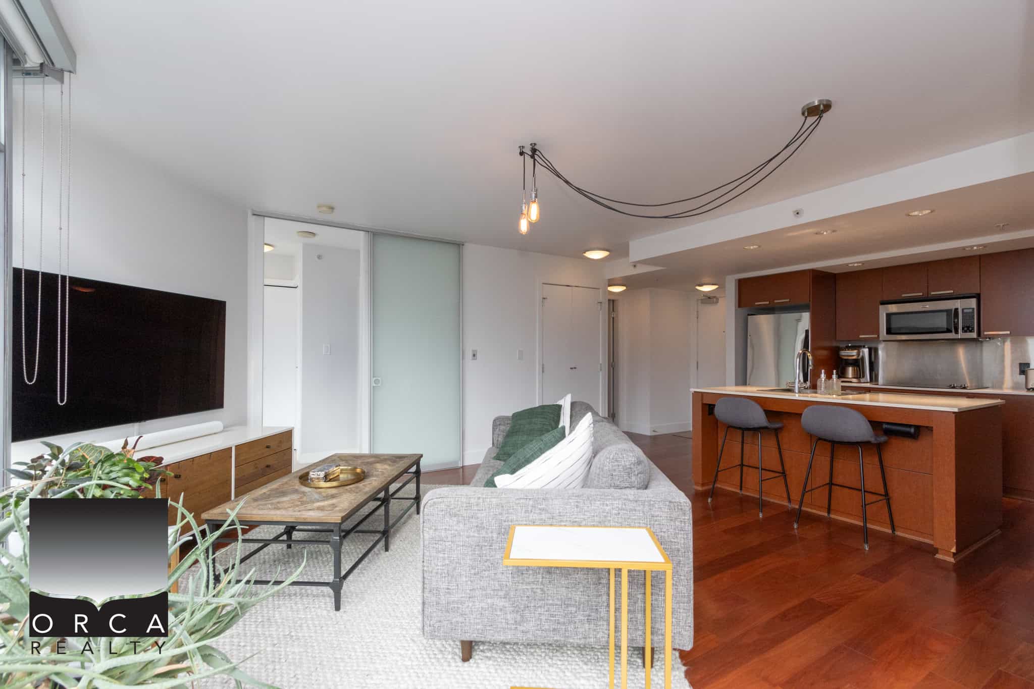 Bright modern condo interior with an open-concept living room and kitchen, featuring sleek appliances, hardwood floors, and contemporary furnishings, ideal for Vancouver real estate buyers.