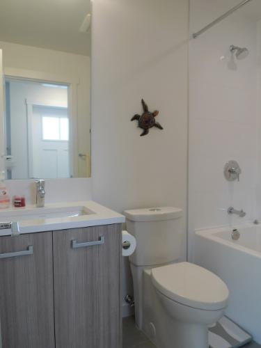 Modern bathroom with a standard toilet, bathtub, and vanity sink, featuring clean white walls and a decorative sea turtle wall art, ideal for showcasing real estate features in Orca Realty Inc. listings.